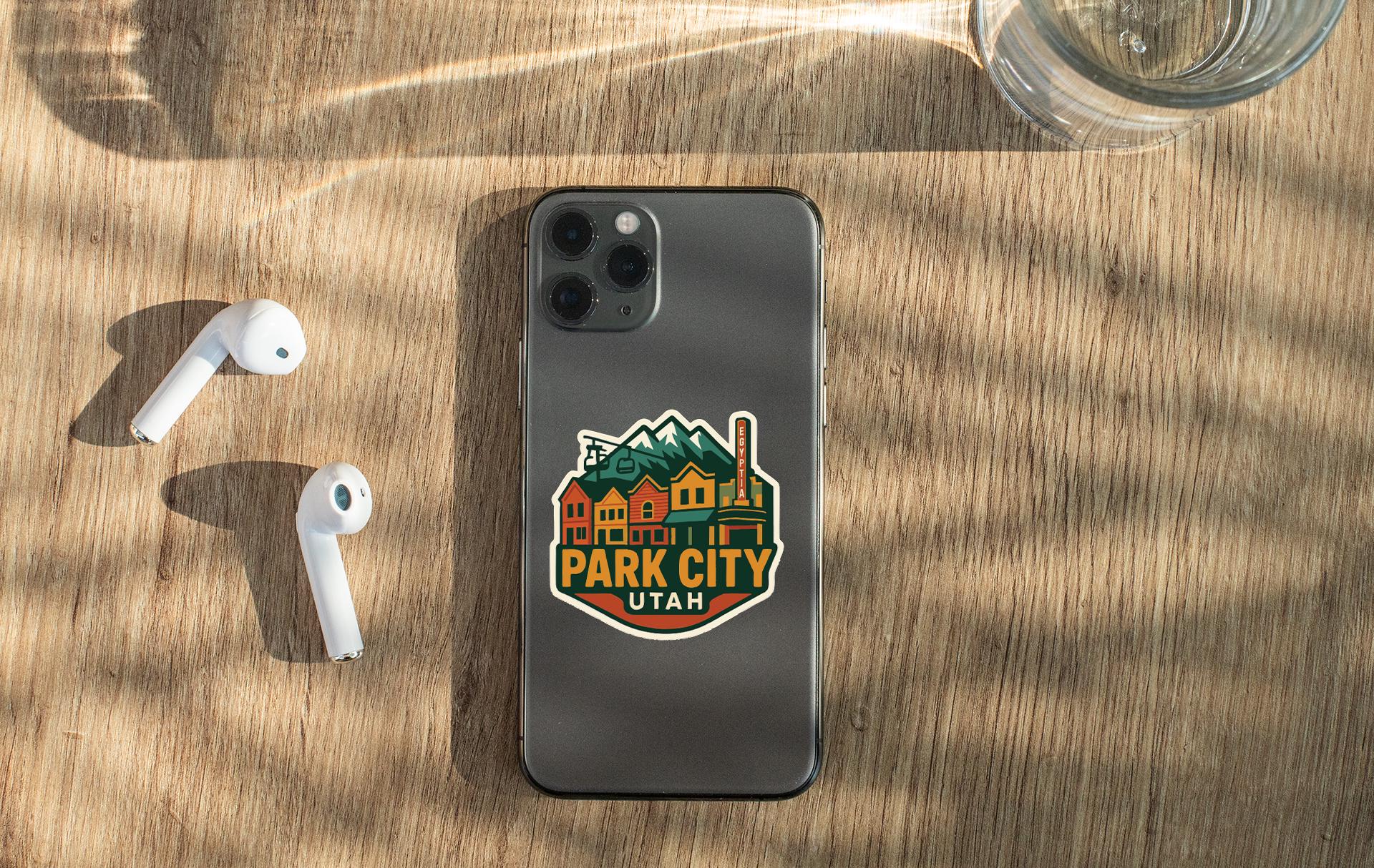 a smartphone with a sticker on the back, placed on a wooden surface alongside a pair of white earbuds and a glass of water.