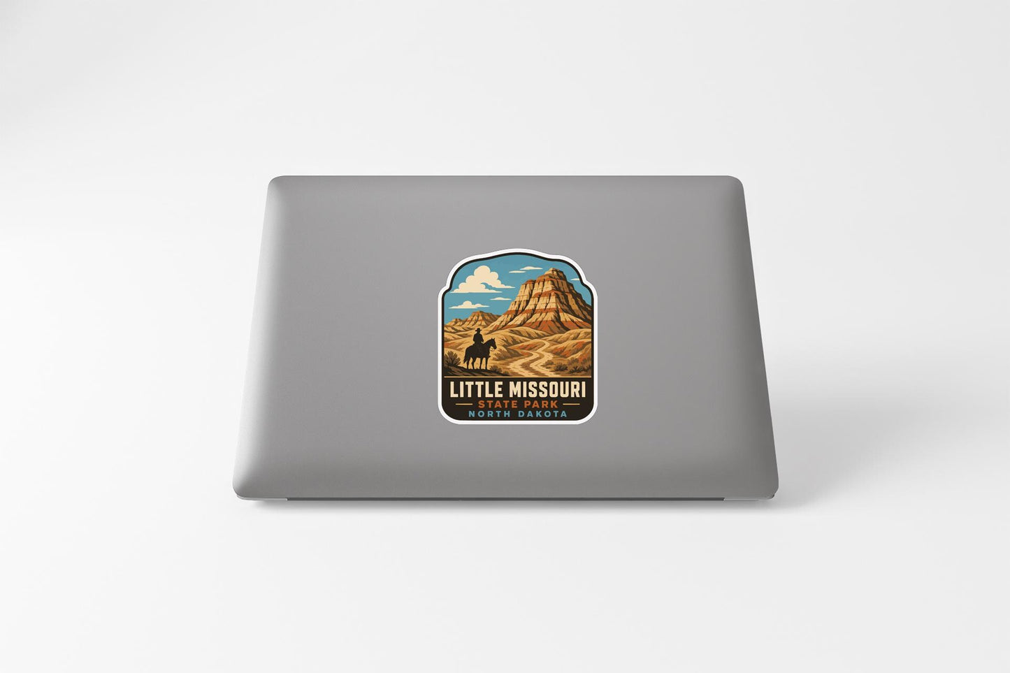 A sticker on the back of a laptop that features an illustration of a mountain landscape with a cowboy riding a horse.