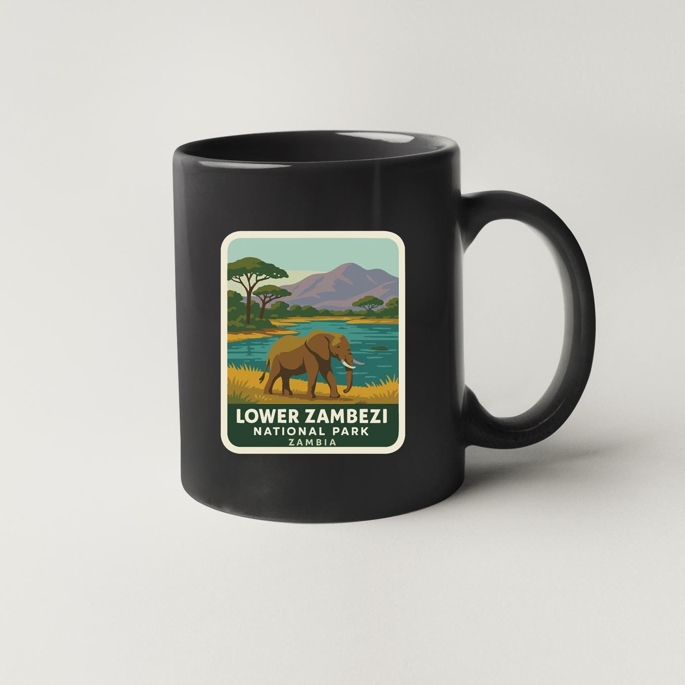 A black coffee mug with a graphic design depicting an elephant in a grassy field near a body of water, with mountains in the background.