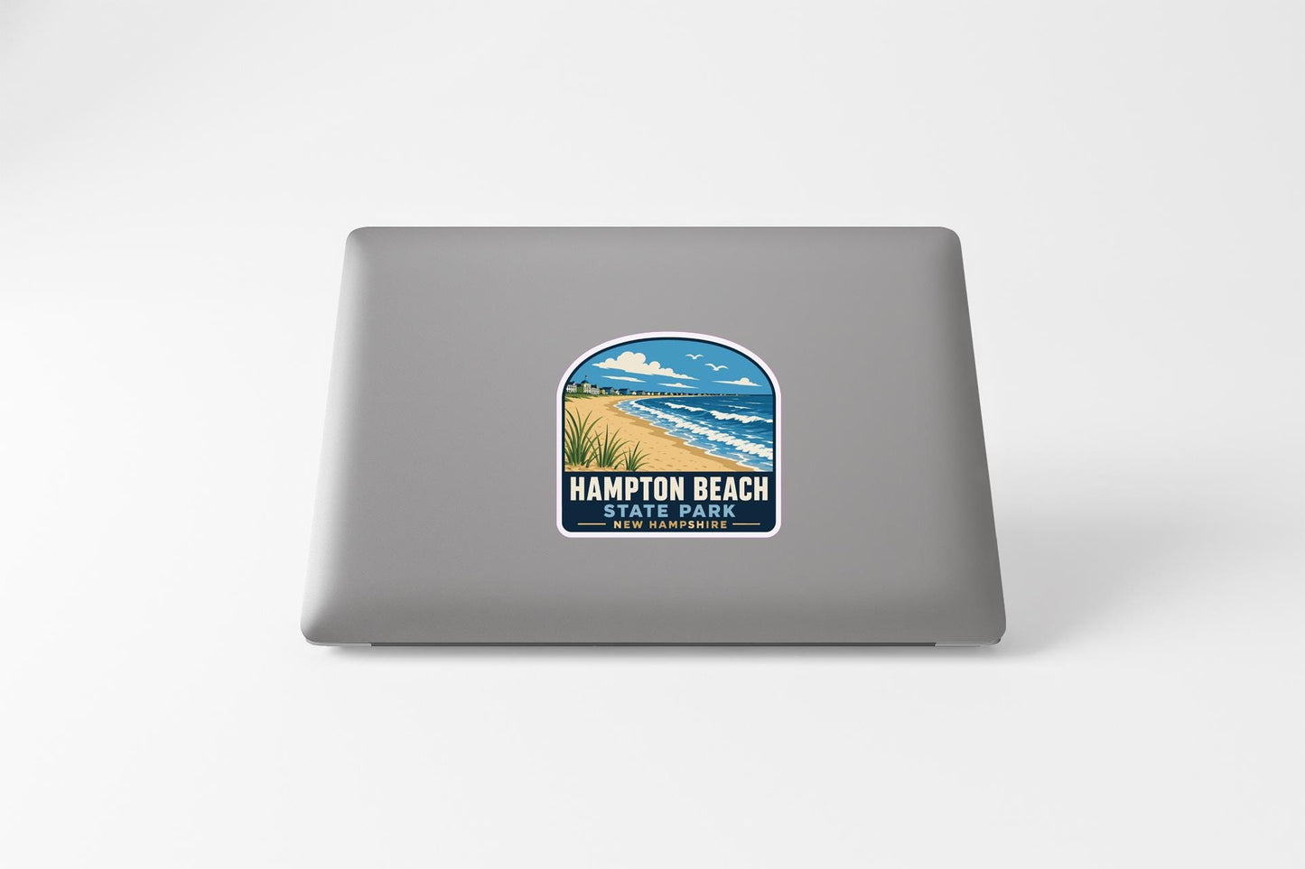 A sticker on the back of a laptop, depicting a beach scene with a body of water and a sandy beach.