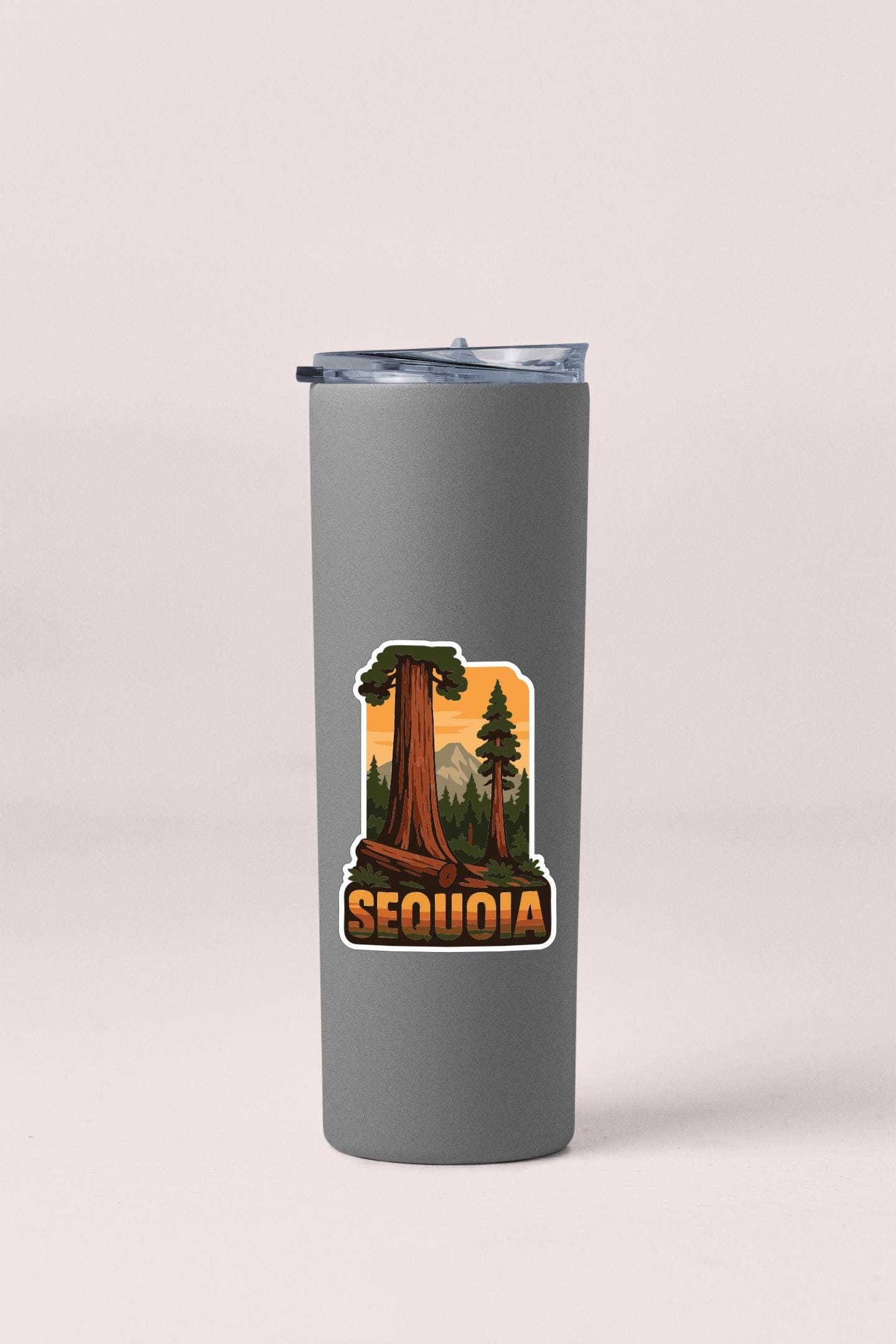 A gray insulated tumbler with a sticker depicting a scenic landscape featuring a sequoia tree and mountains.