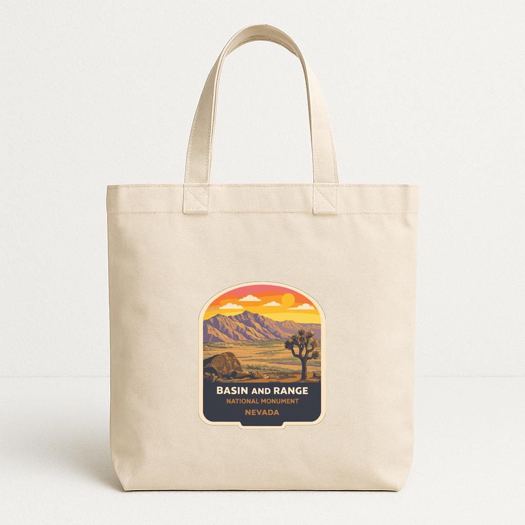 A beige tote bag with a graphic design depicting a desert landscape with mountains, a tree, and a sunset.