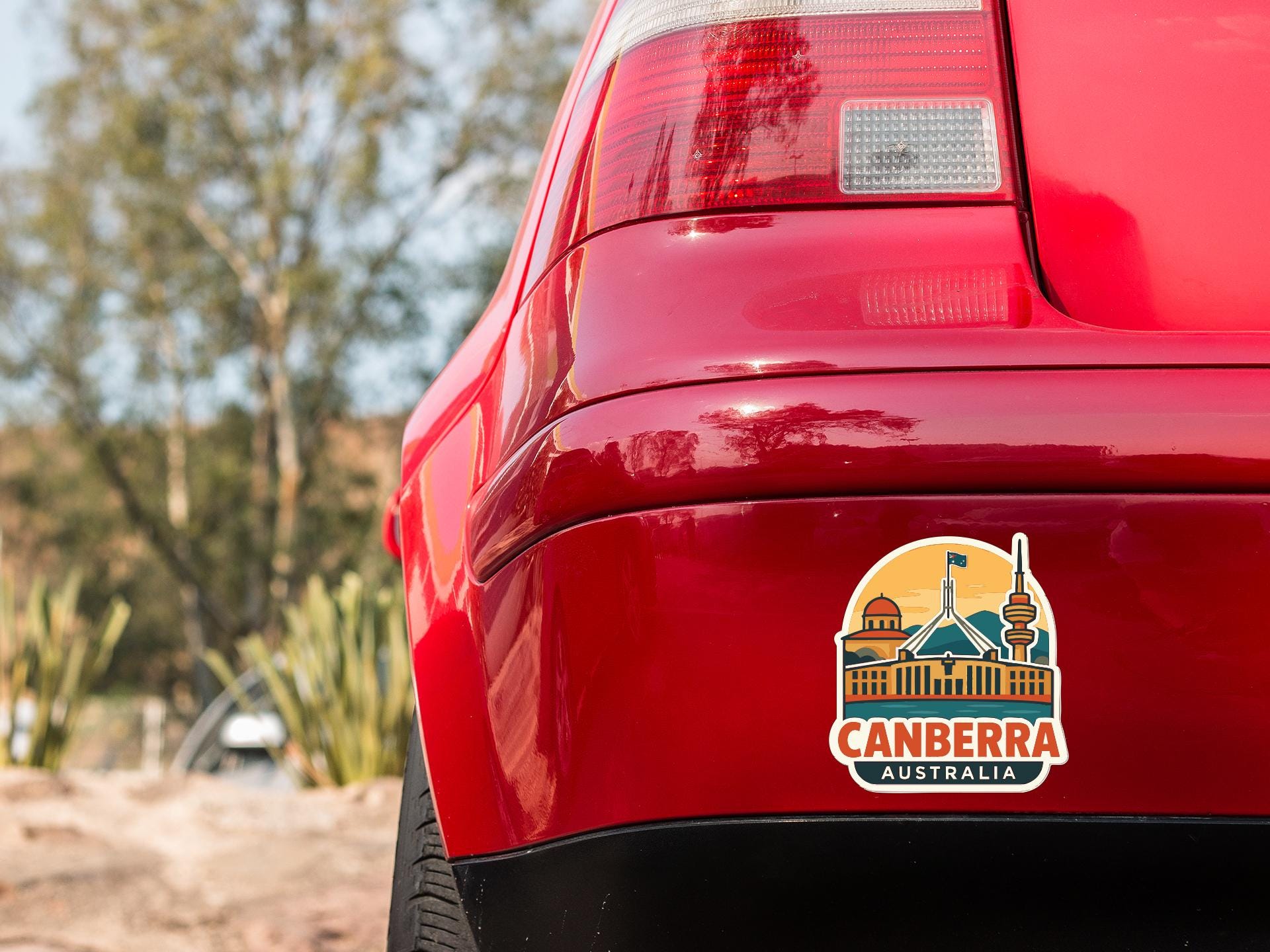 the rear end of a red car with a sticker on the trunk that says "CANBERRA AUSTRALIA".
