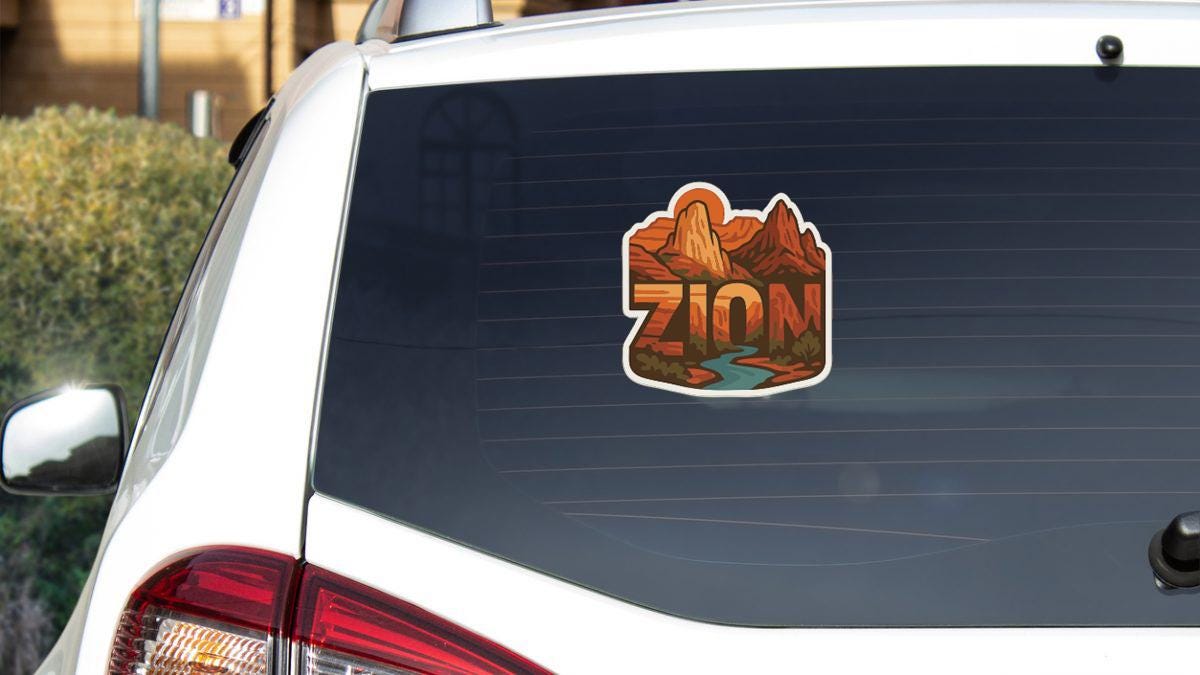 the rear window of a white car with a sticker featuring a mountain landscape and the word "ZION" printed on it.