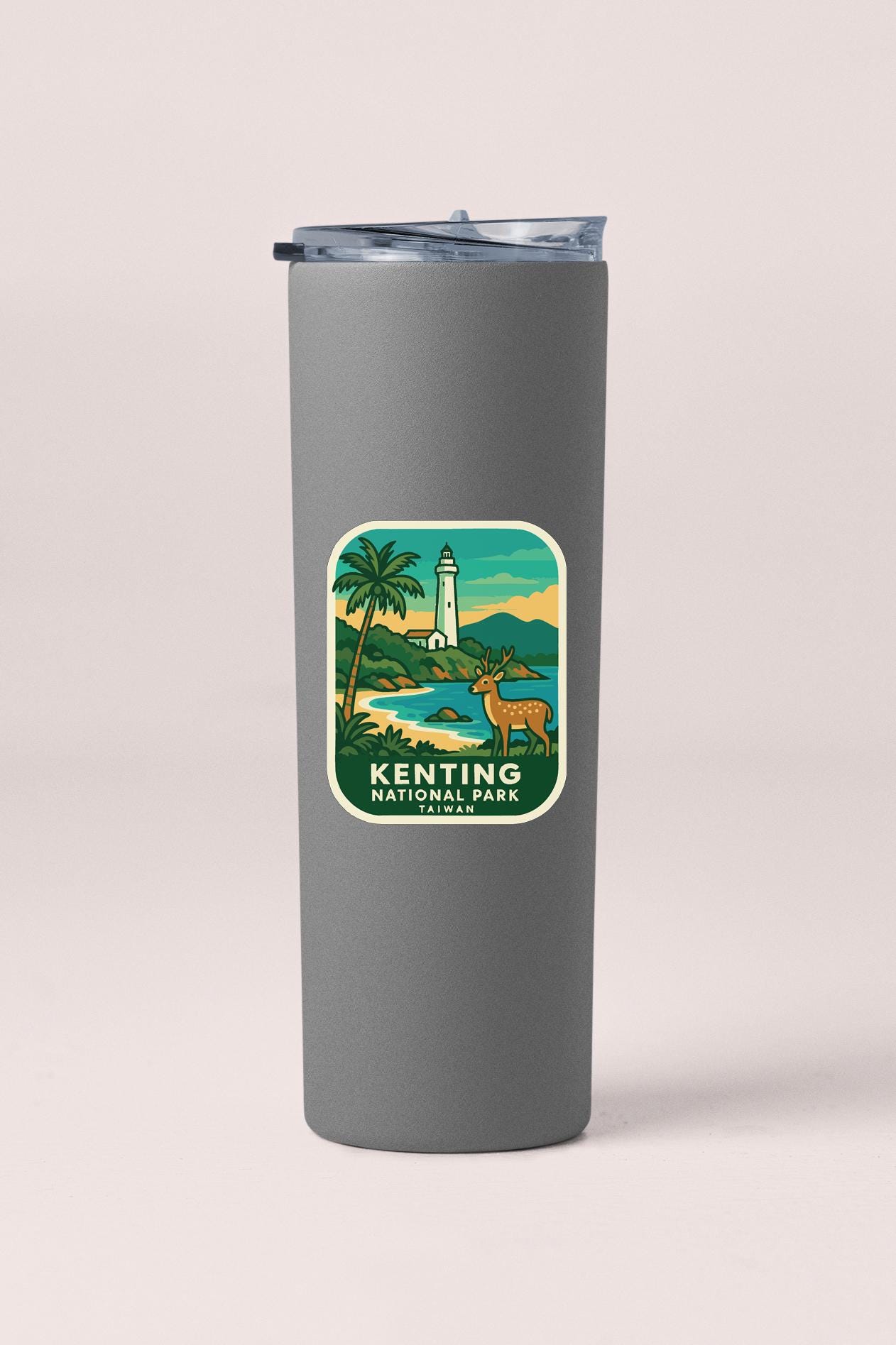 A gray insulated tumbler with a label that features an illustration of a lighthouse and a deer in a tropical landscape.