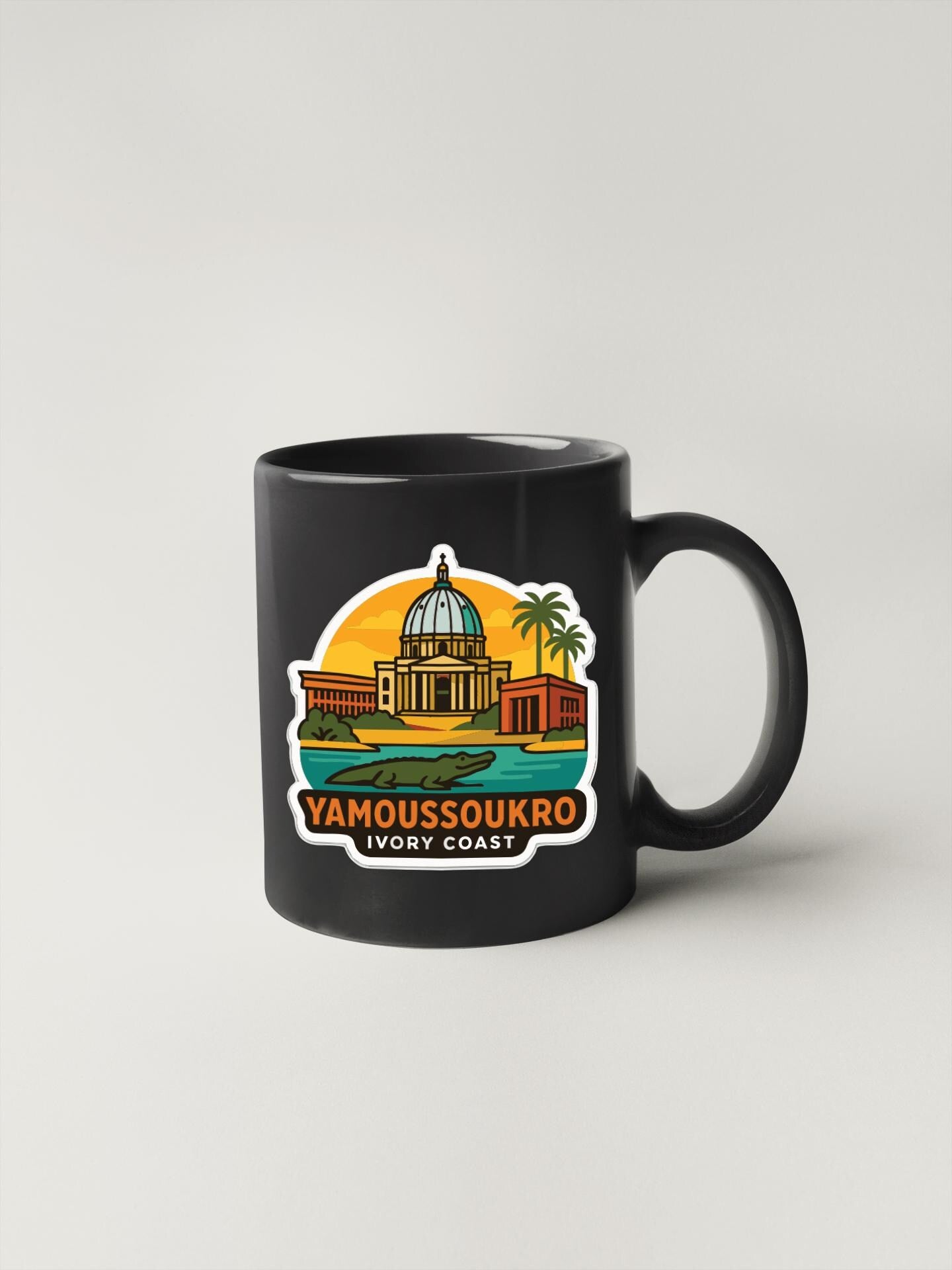 A black coffee mug with a colorful illustration of a building and palm trees, along with the text "YAMOUSOUKRO VIRGINIA COAST".