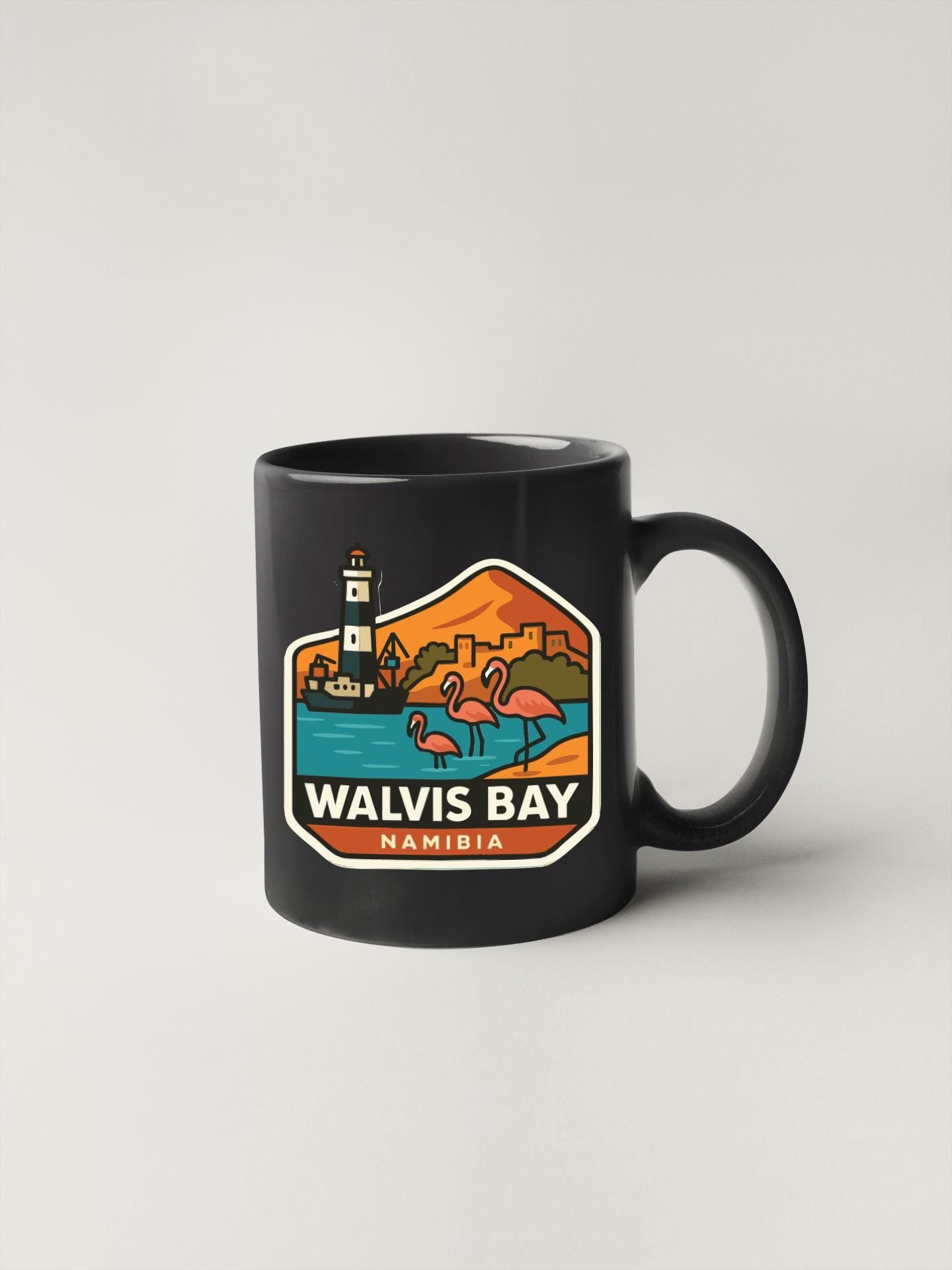 A black coffee mug with a colorful graphic depicting a lighthouse, flamingos, and a beach scene, along with the text "WALVIS BAY NAMIBIA".