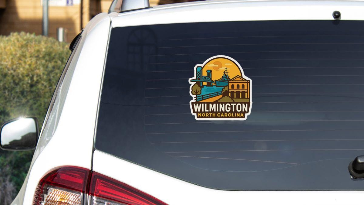 A sticker on the rear window of a white car, depicting a cityscape with a bridge and buildings, along with the text "Wilmington North Carolina".
