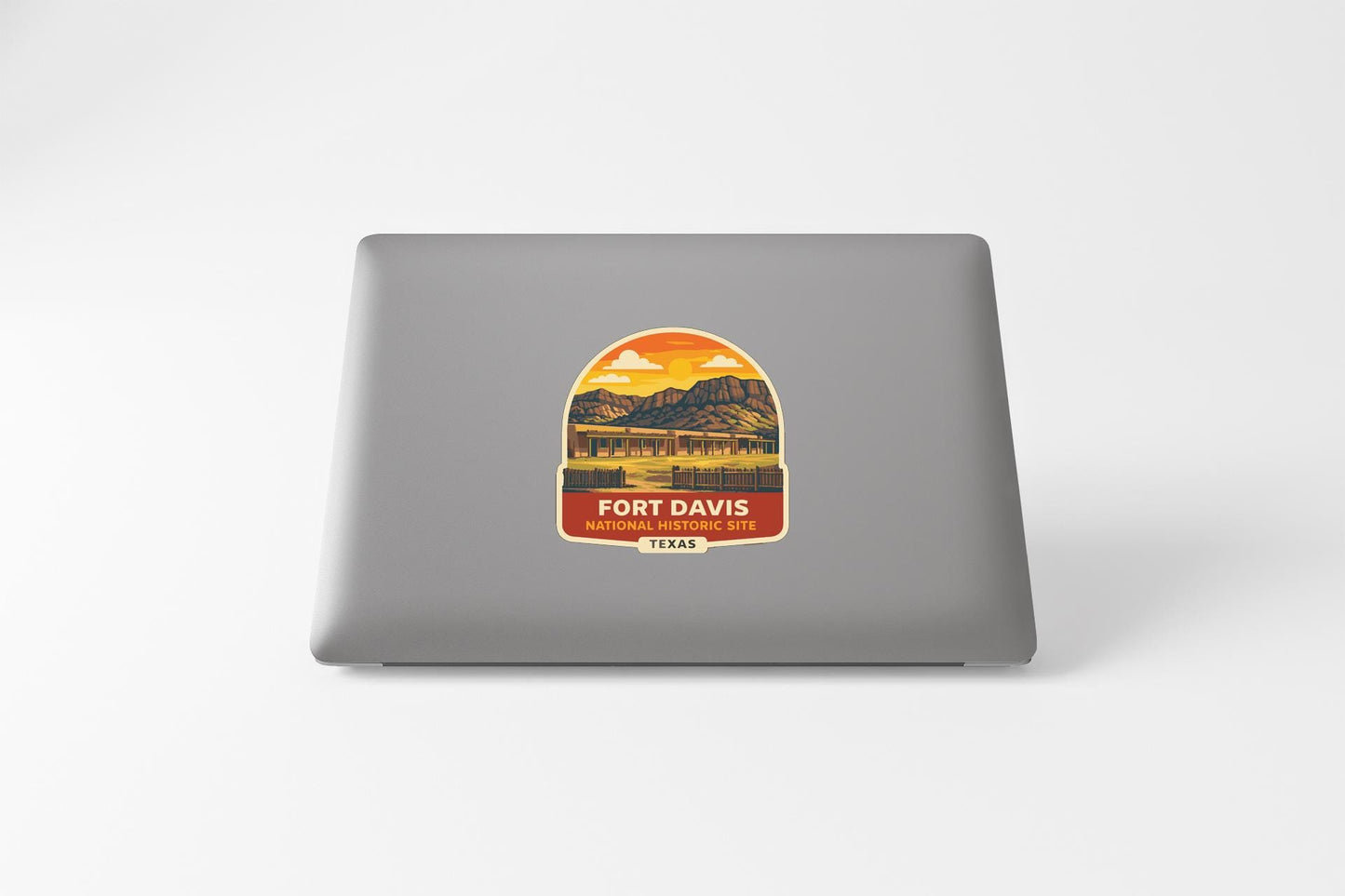 a sticker or decal on the back of a laptop, depicting a scenic landscape with mountains and a sunset.