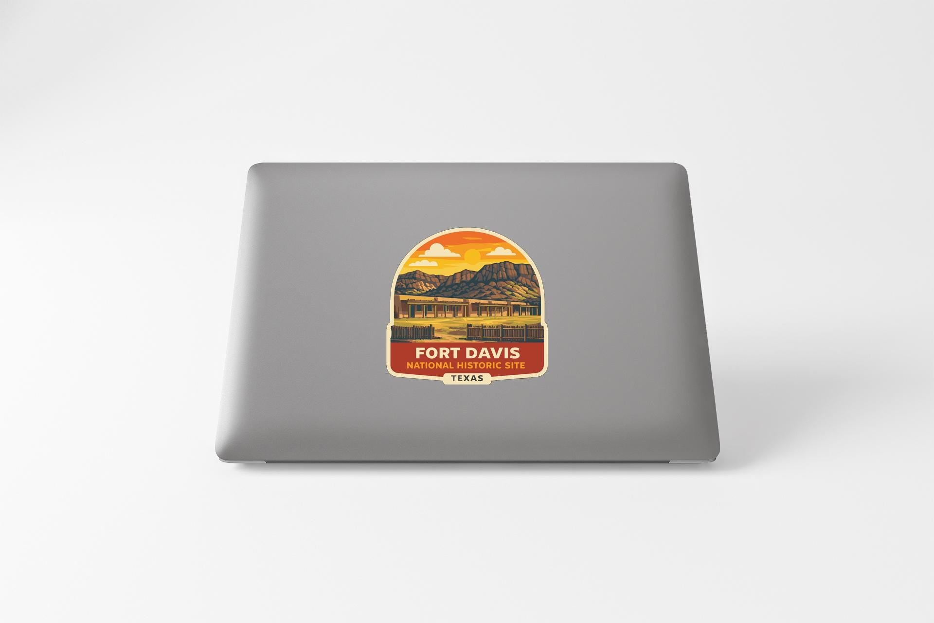 a sticker or decal on the back of a laptop, depicting a scenic landscape with mountains and a sunset.