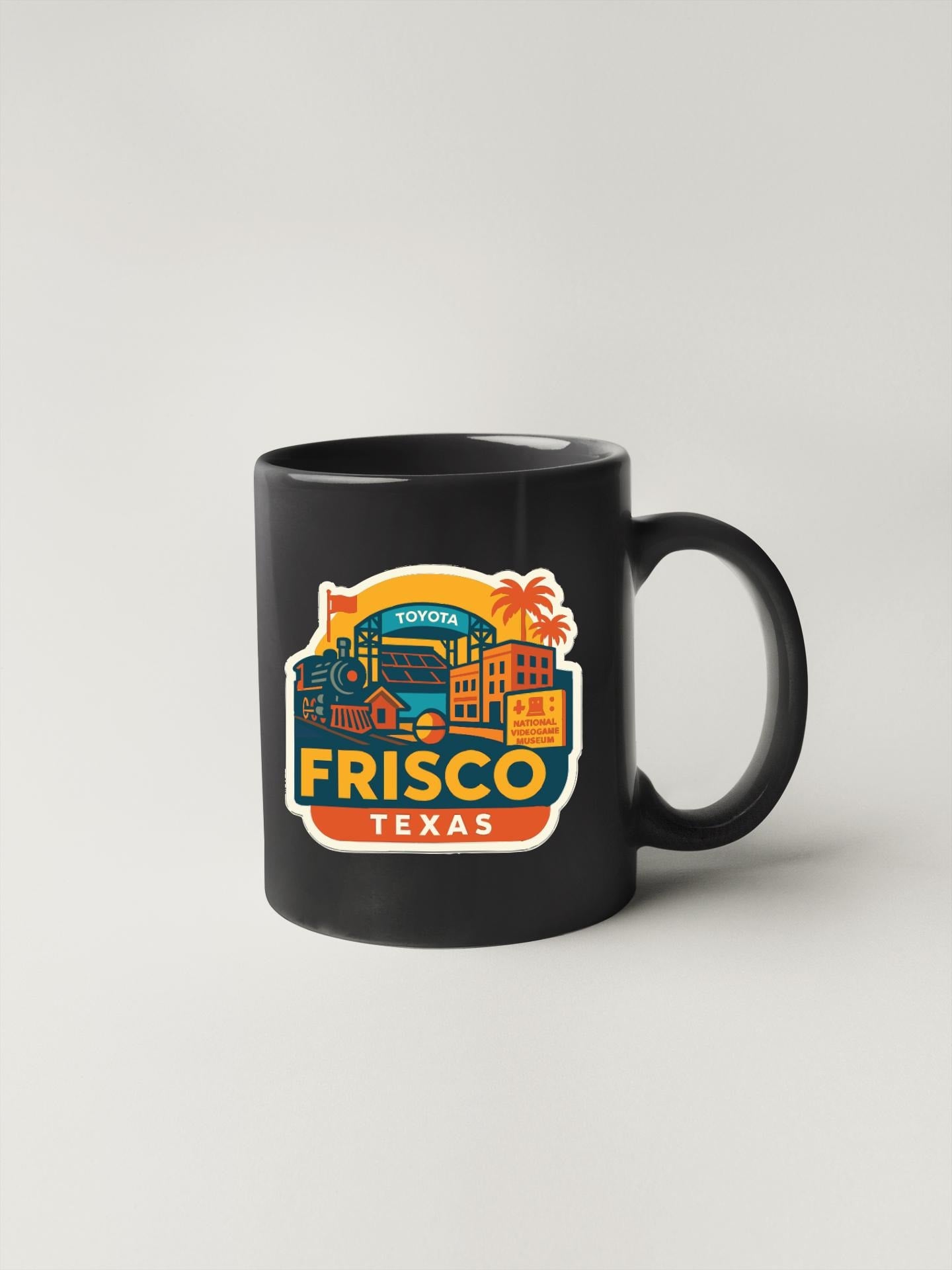 A black coffee mug with a colorful graphic design featuring the text "TOYOTA FRISCO TEXAS" and various cityscape elements.
