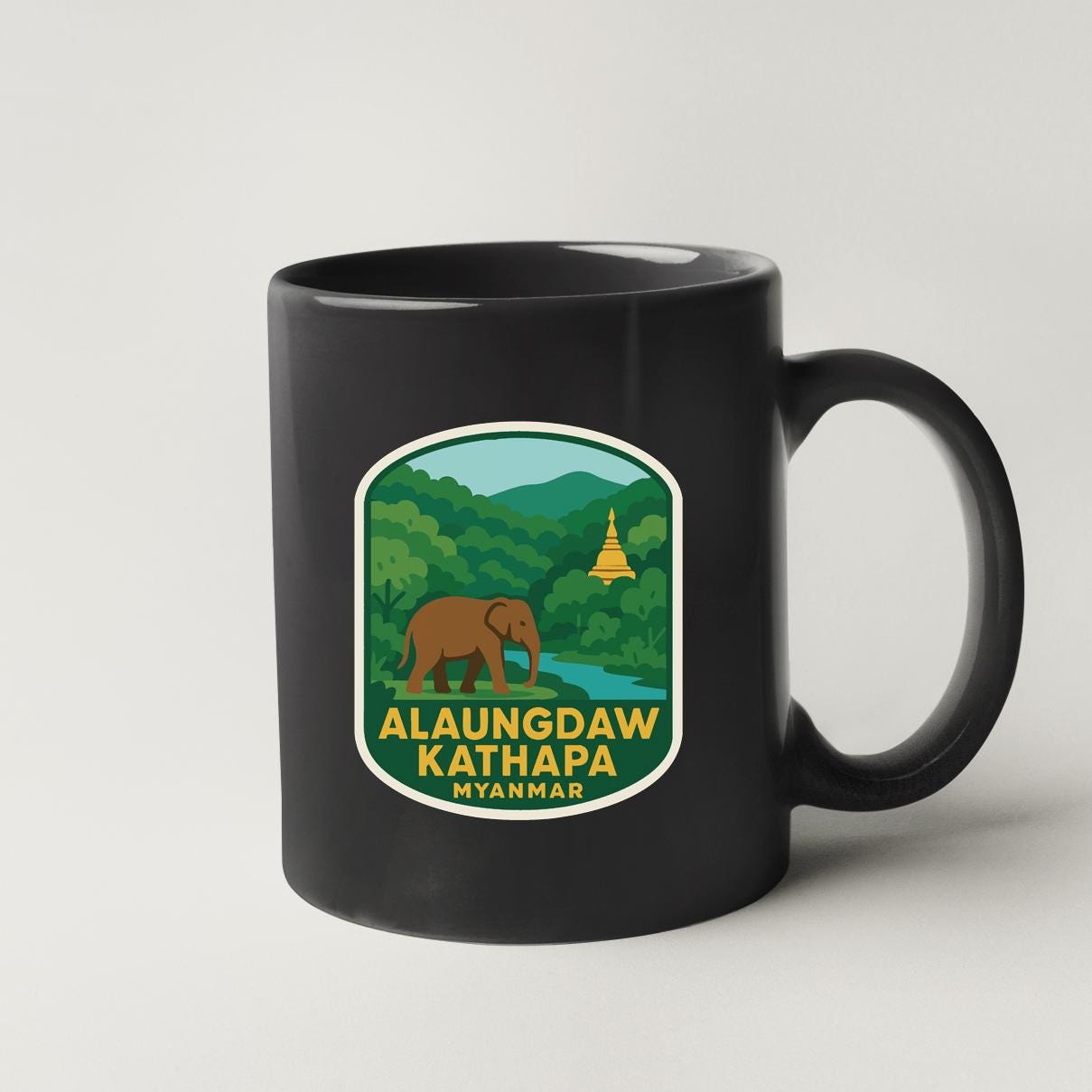 A black coffee mug with a label that features an illustration of an elephant and a temple in a lush, green landscape.