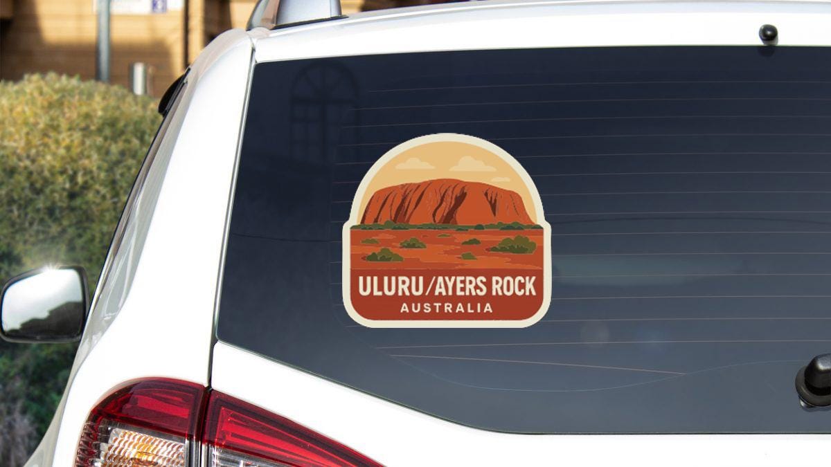 A sticker on the rear window of a car, depicting Uluru, a famous landmark in Australia.