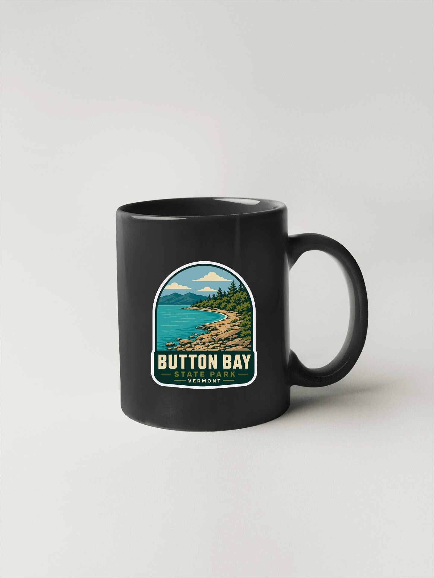 A black coffee mug with a graphic design depicting a scenic landscape, including a body of water, mountains, and trees.