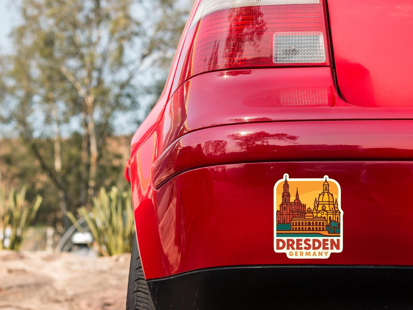 the rear end of a red car with a sticker on the trunk that displays the name 'Dresden, Germany'.