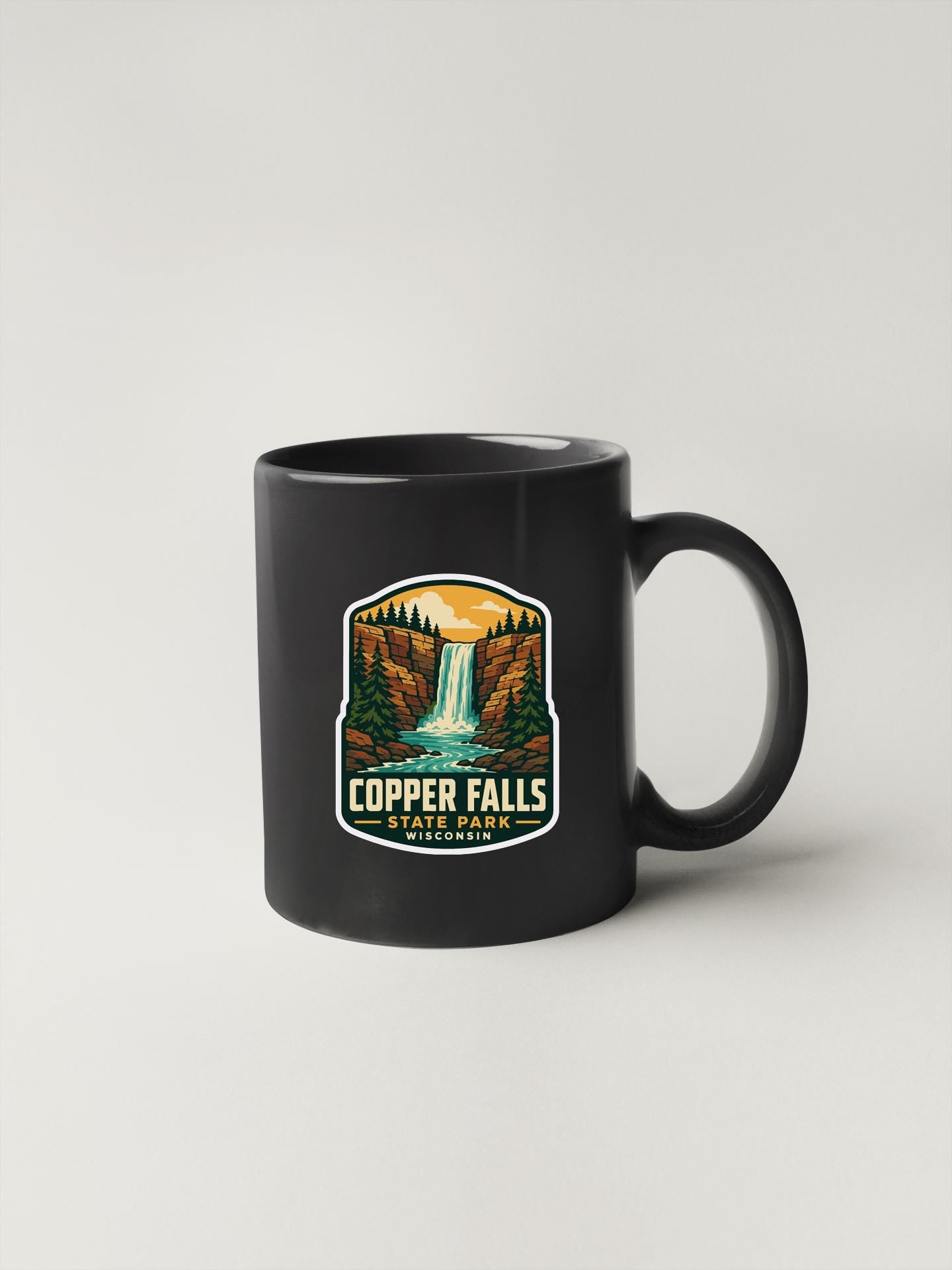 A black coffee mug with a sticker depicting Copper Falls State Park in California.