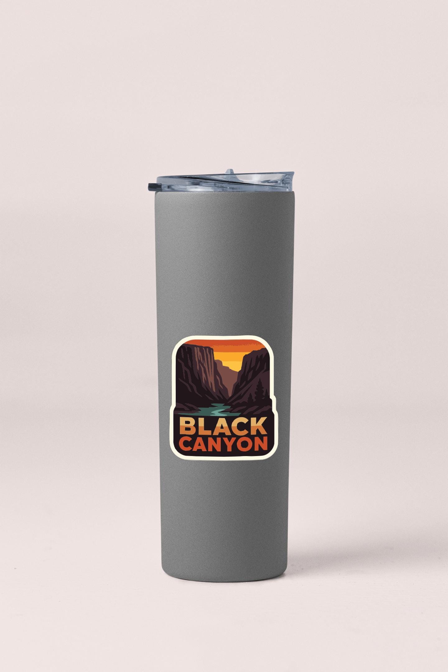 A gray tumbler with a sticker depicting a scenic mountain landscape, specifically Black Canyon.