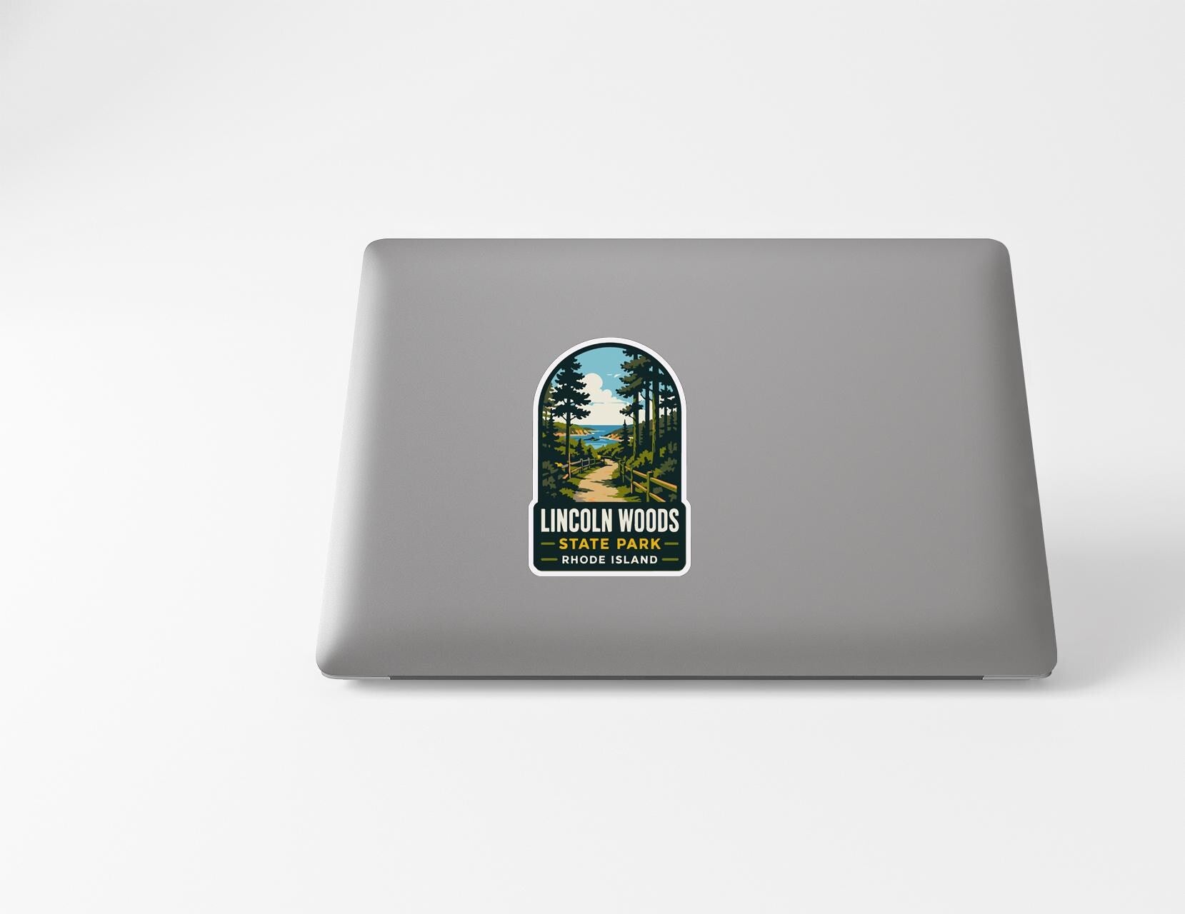 A sticker on the back of a laptop, depicting a scenic landscape with a path leading through a forest.