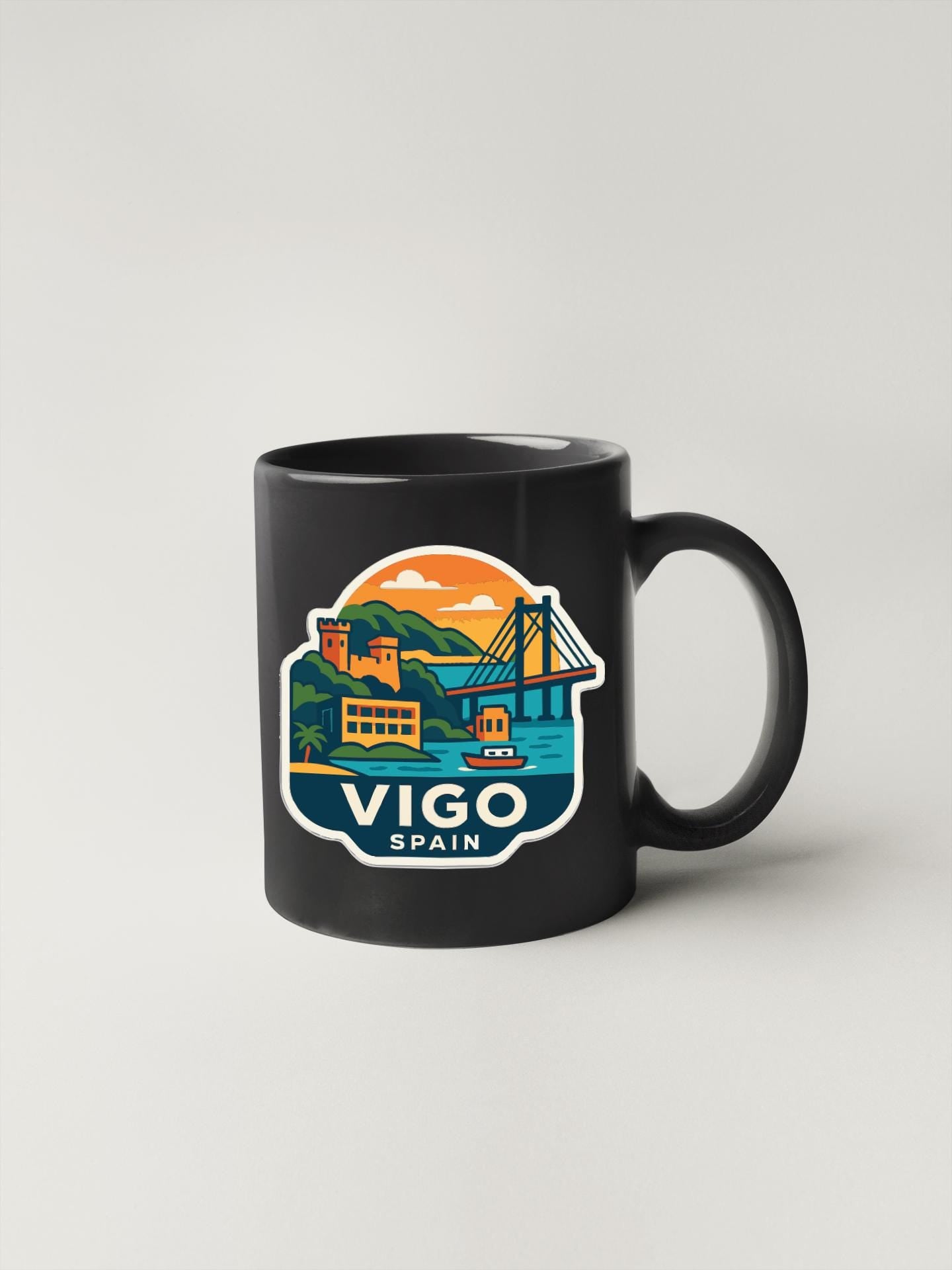 A black coffee mug with a colorful illustration of a coastal town and a bridge, along with the text "Vigo, Spain" printed on it.