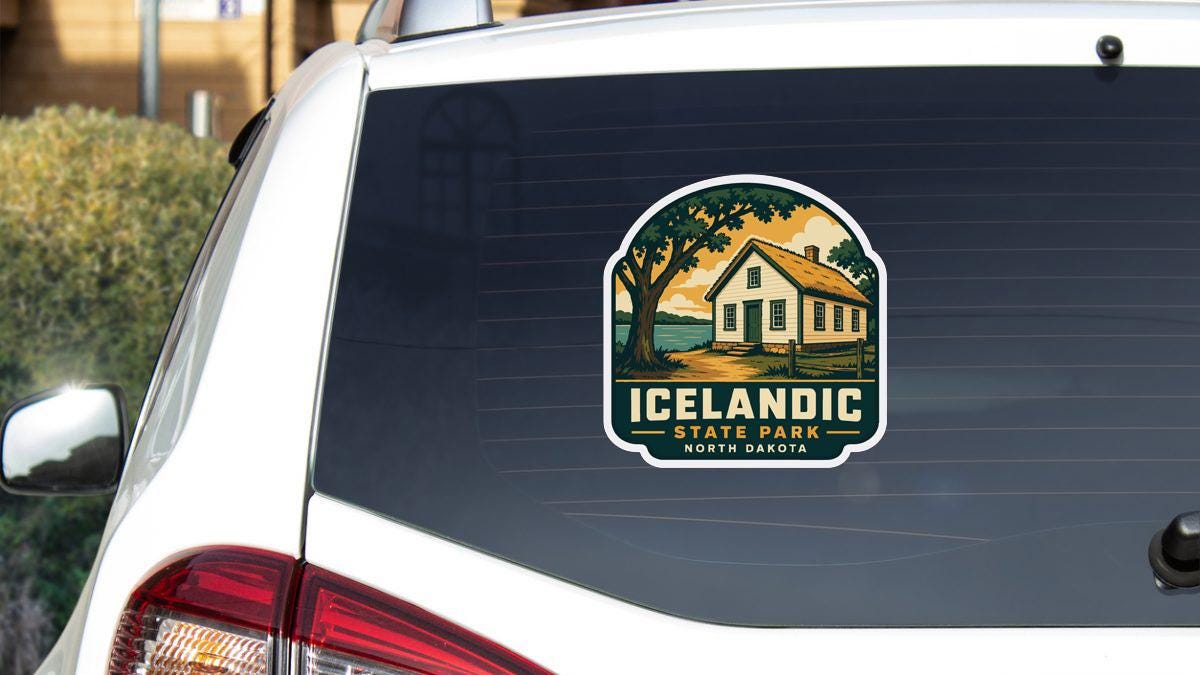 A sticker on the rear window of a white vehicle, depicting a house and trees, with the text "ICELANDIC STATE PARK NORTH DAKOTA" printed on it.