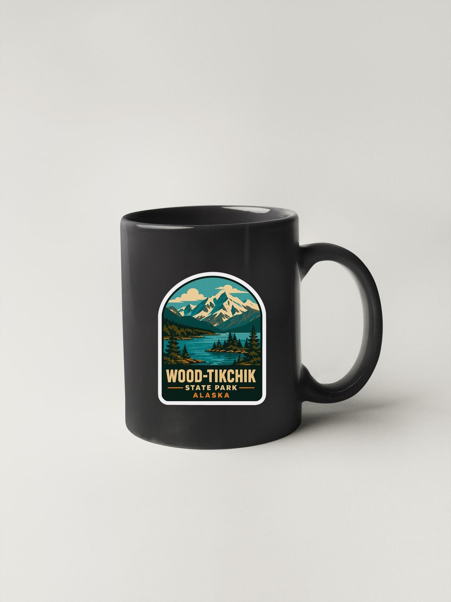 A black coffee mug with a sticker depicting a scenic mountain landscape and the text "WOOD-TIKCHIK STATE PARK OREGON".