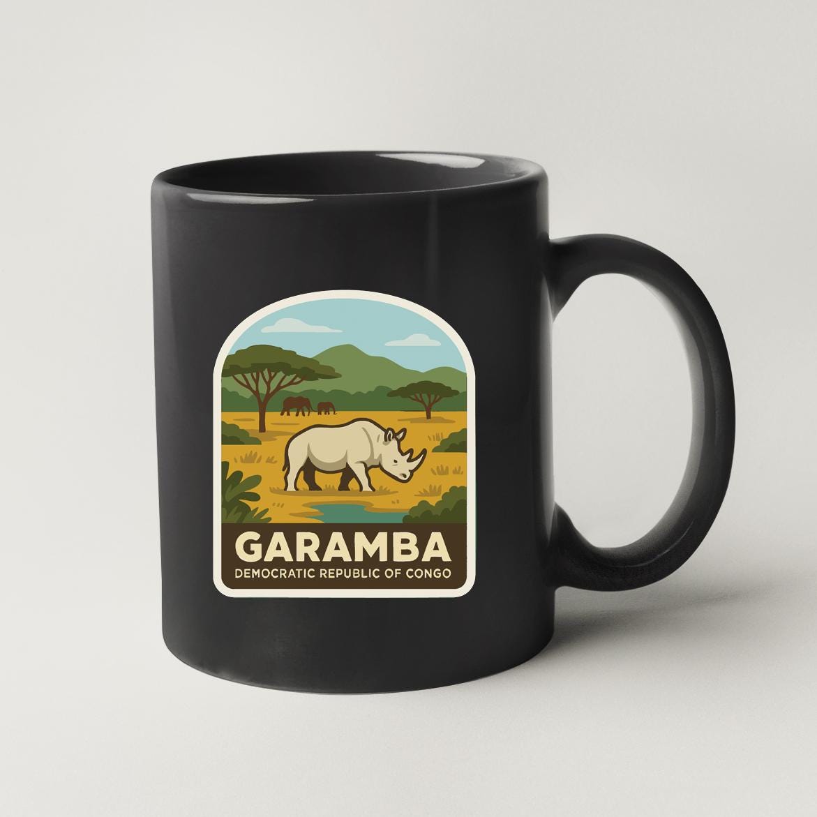 A black coffee mug with a graphic design depicting a rhinoceros in a savanna landscape, along with the text "GARAMBA DEMOCRATIC REPUBLIC OF CONGO".