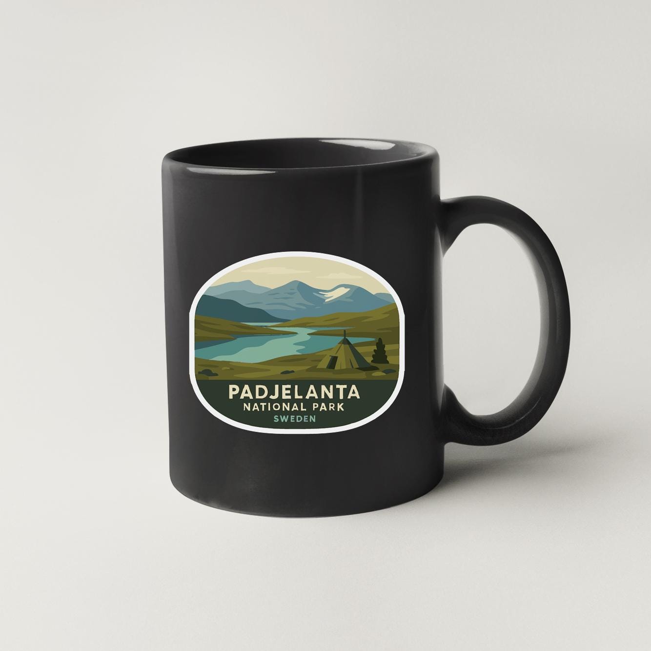 A black coffee mug with a sticker depicting the scenic landscape of Padjelanta National Park in Sweden.