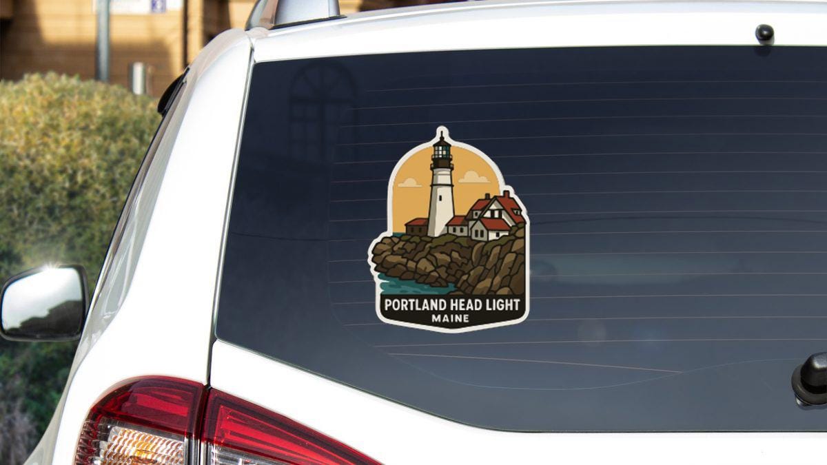 A sticker on the rear window of a car depicting a lighthouse and a coastal town, with the text "PORTLAND HEAD LIGHT MAINE" below it.