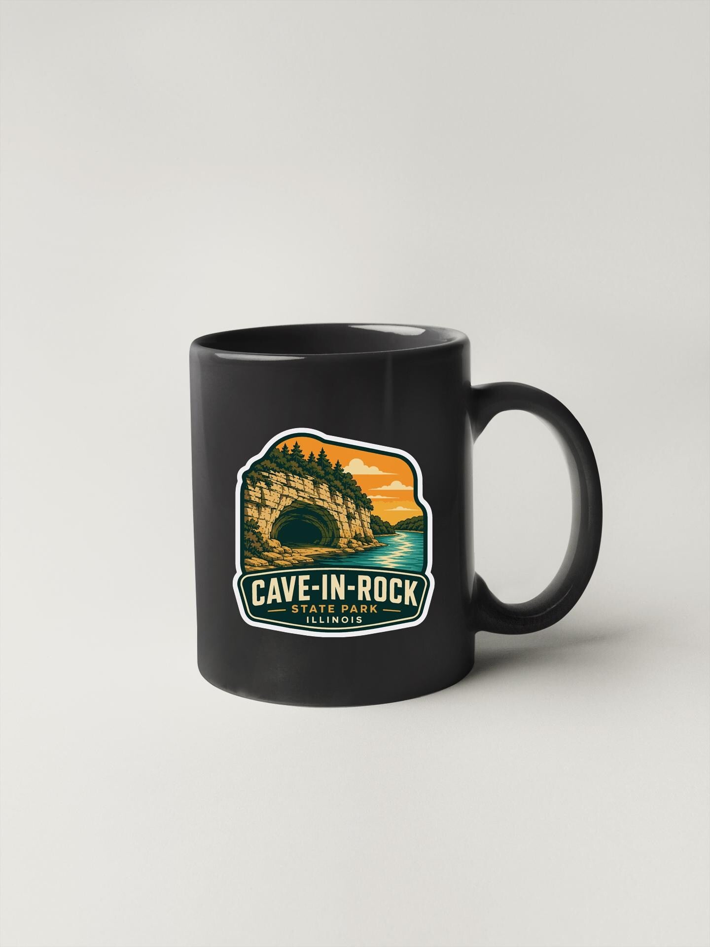 A black coffee mug with a graphic design depicting a cave in a rock formation, along with the text "CAVE-IN-ROCK" and "STILLINOIS".