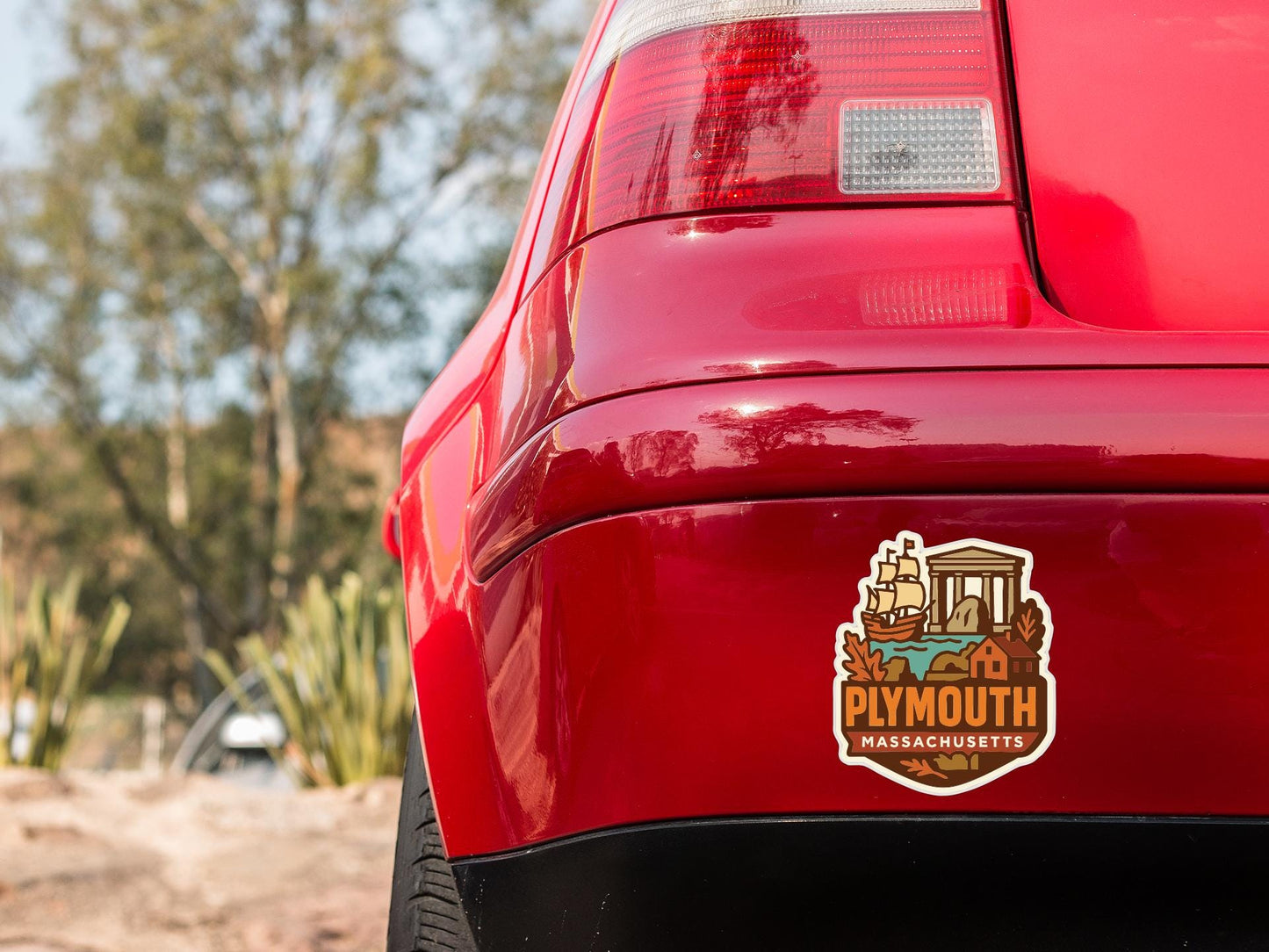 the rear end of a red car with a sticker on it, featuring a ship and the text "Plymouth Massachusetts".
