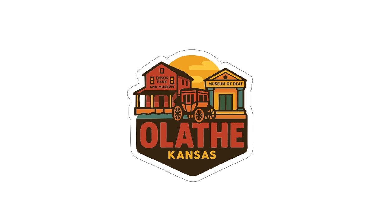 A sticker or emblem featuring a stylized illustration of a building with a wagon in front of it, along with the text "OLATHE KANSAS" prominently displayed.