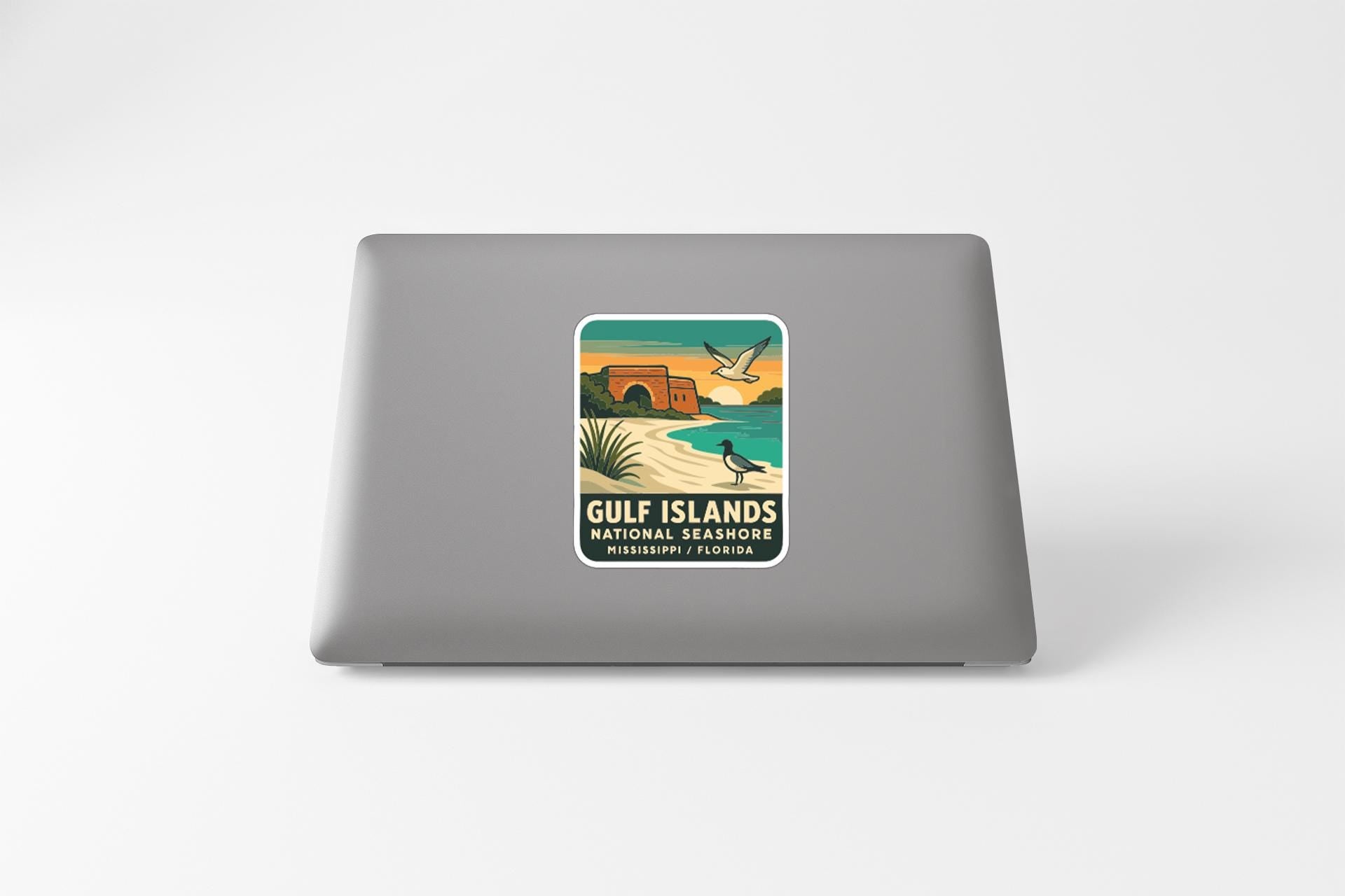 A sticker on the back of a laptop, depicting a beach scene with palm trees, a bird, and a building.