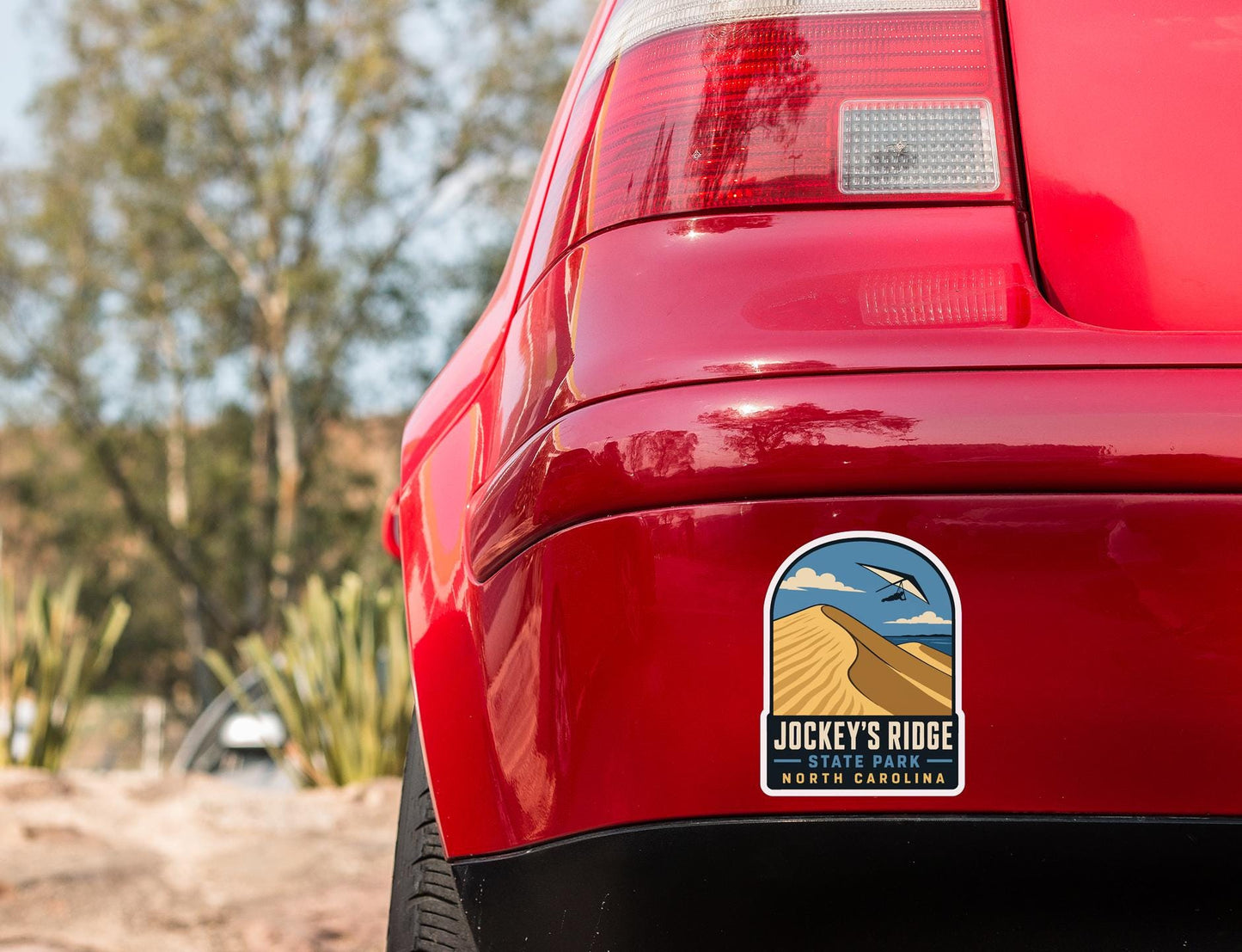 the rear end of a red car with a sticker on the trunk that says "Jockey's Ridge State Park North Carolina".