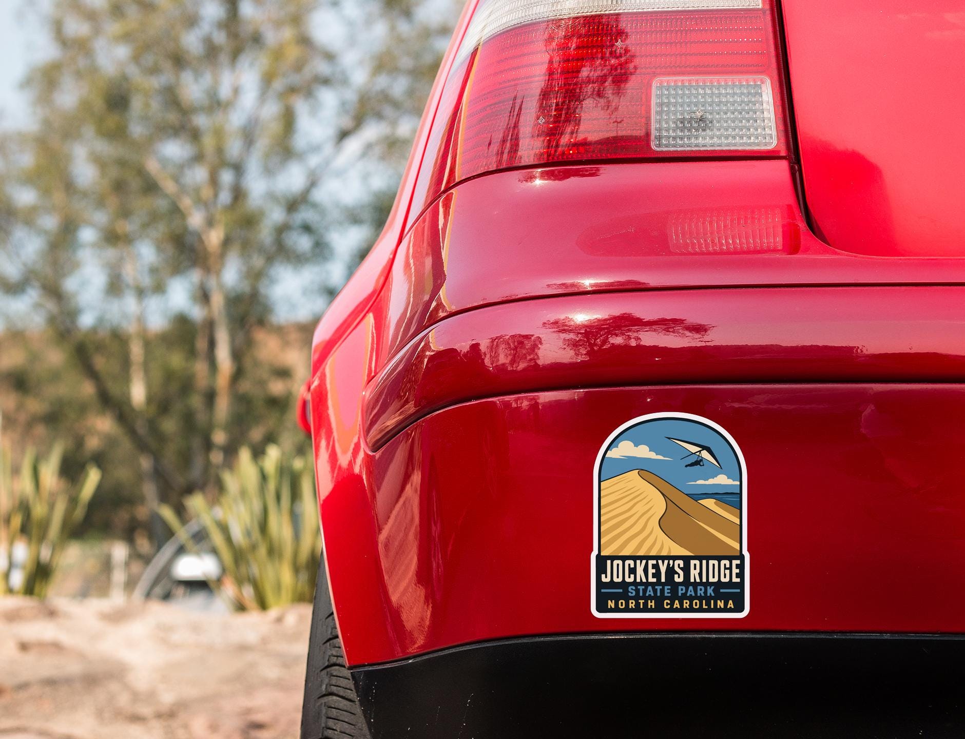 the rear end of a red car with a sticker on the trunk that says "Jockey's Ridge State Park North Carolina".