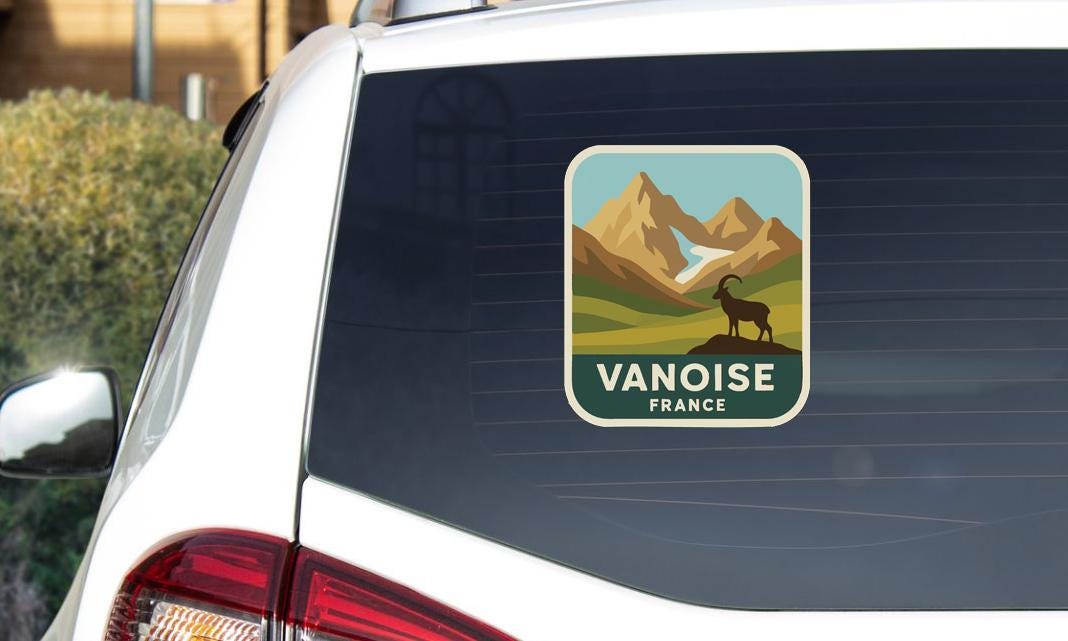 a sticker on the rear window of a white car, depicting a mountain landscape with a goat.