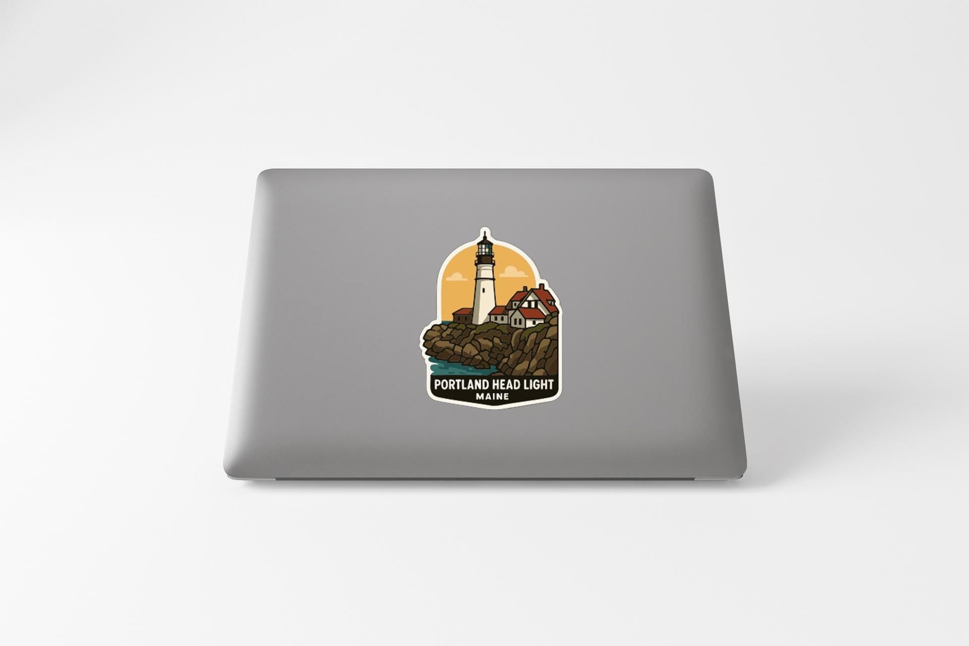 A sticker depicting a lighthouse and a coastal scene, with the text "PORTLAND HEAD LIGHT MAINE" printed on it.