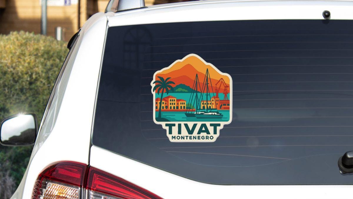 a sticker on the rear window of a car, depicting a scenic view of a coastal town with palm trees, buildings, and a boat on the water.