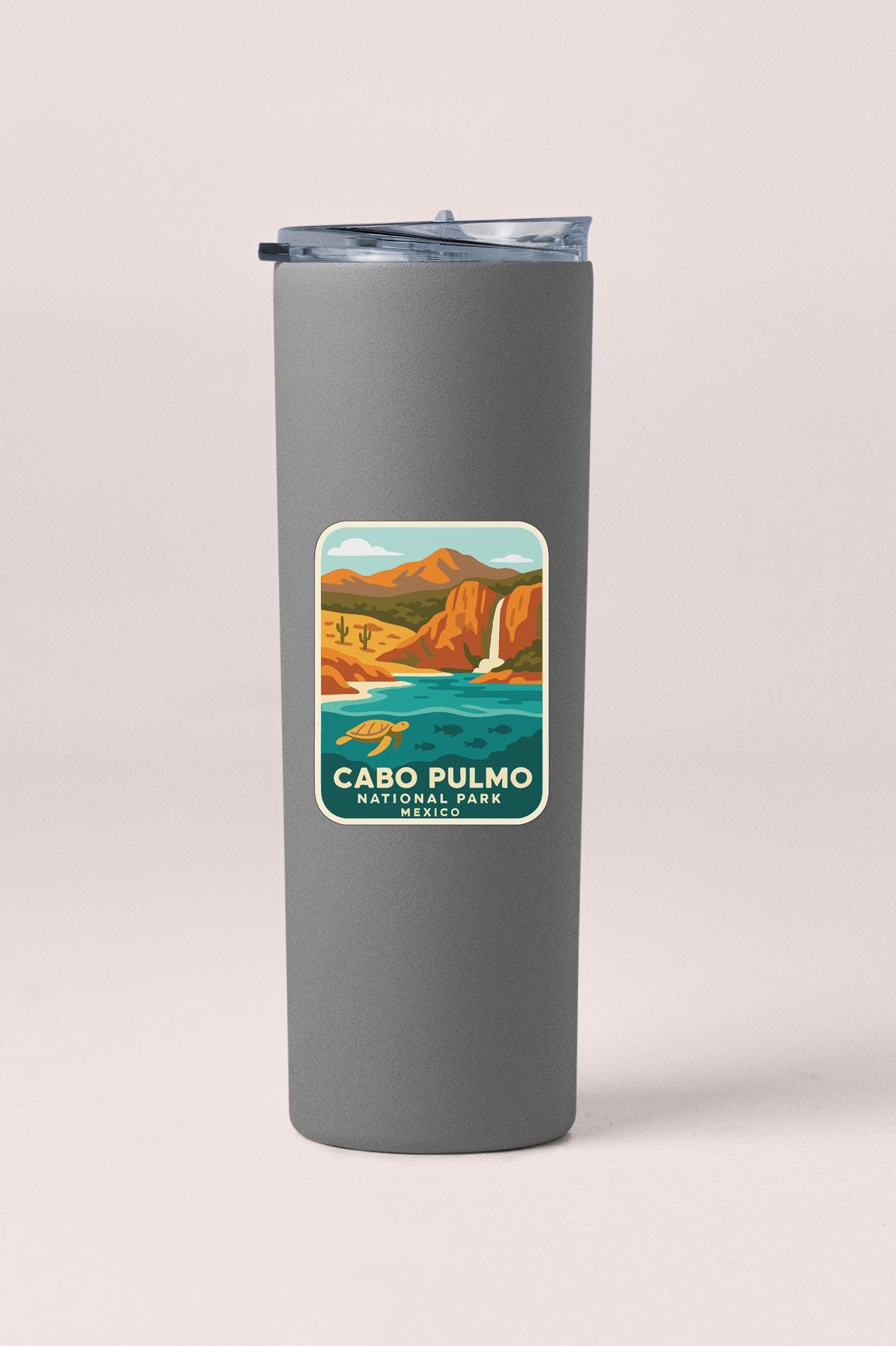 A gray insulated tumbler with a label that features an illustration of a scenic landscape with mountains, water, and desert terrain.