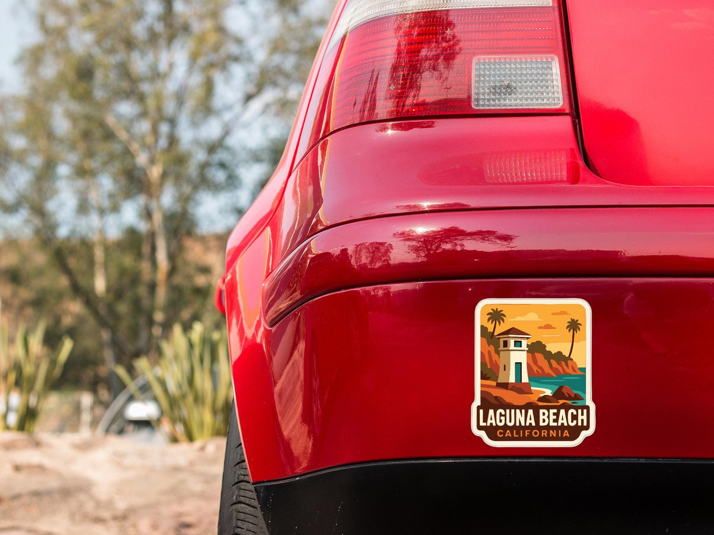 the rear end of a red car with a sticker on the trunk that says "Laguna Beach California".