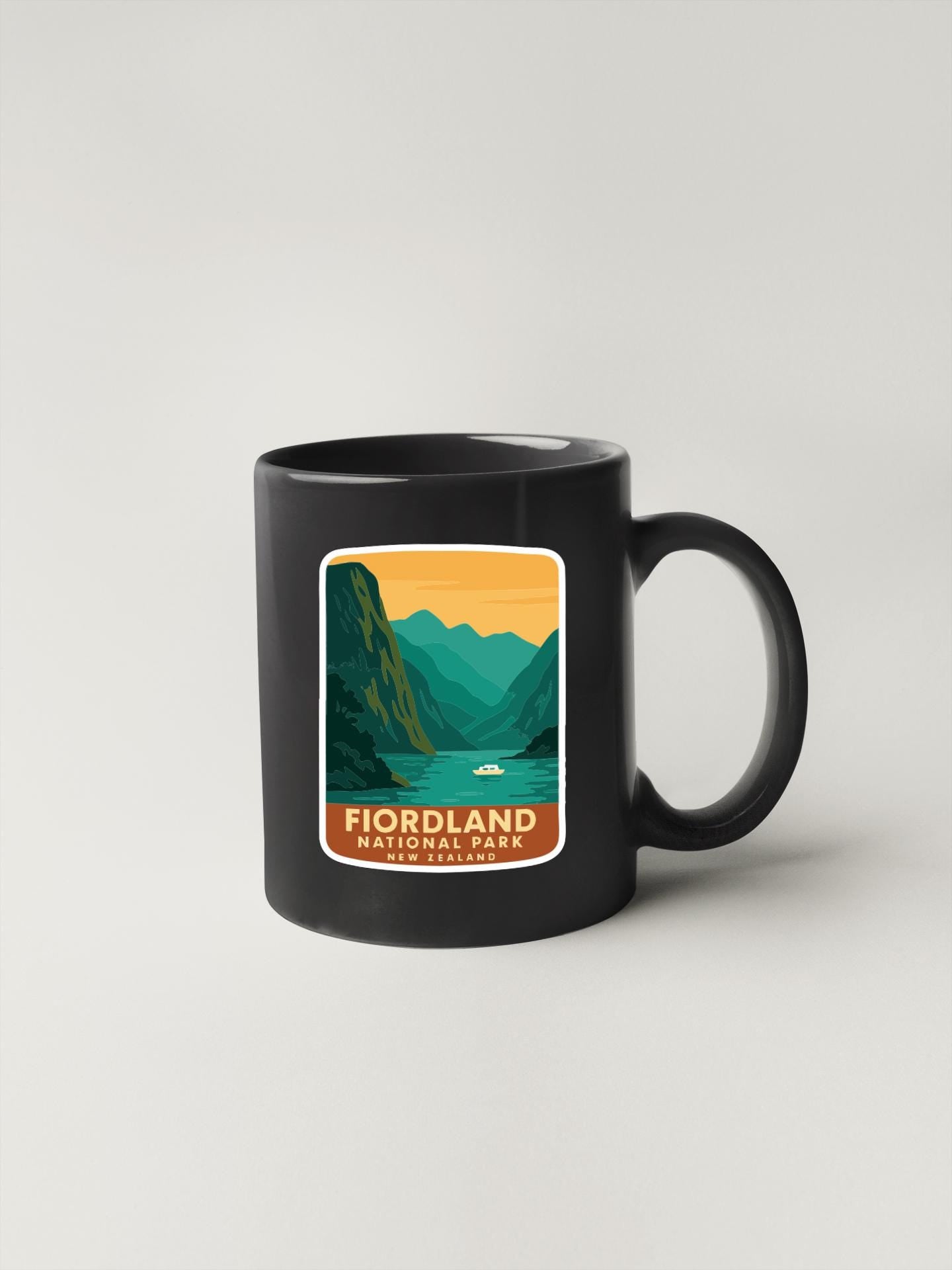 A black coffee mug with a graphic design depicting a mountainous landscape with a lake and a boat.