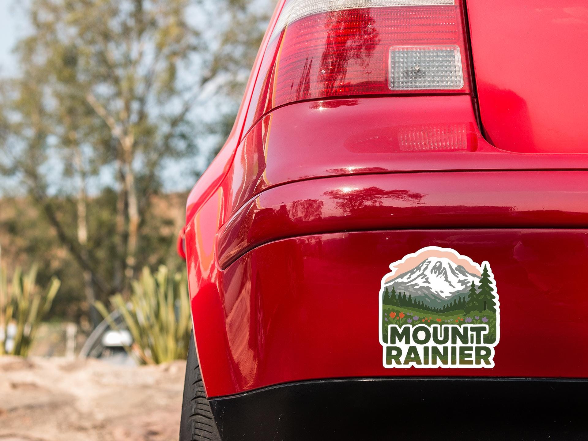 the rear end of a red car with a mountain rainier sticker on the trunk.
