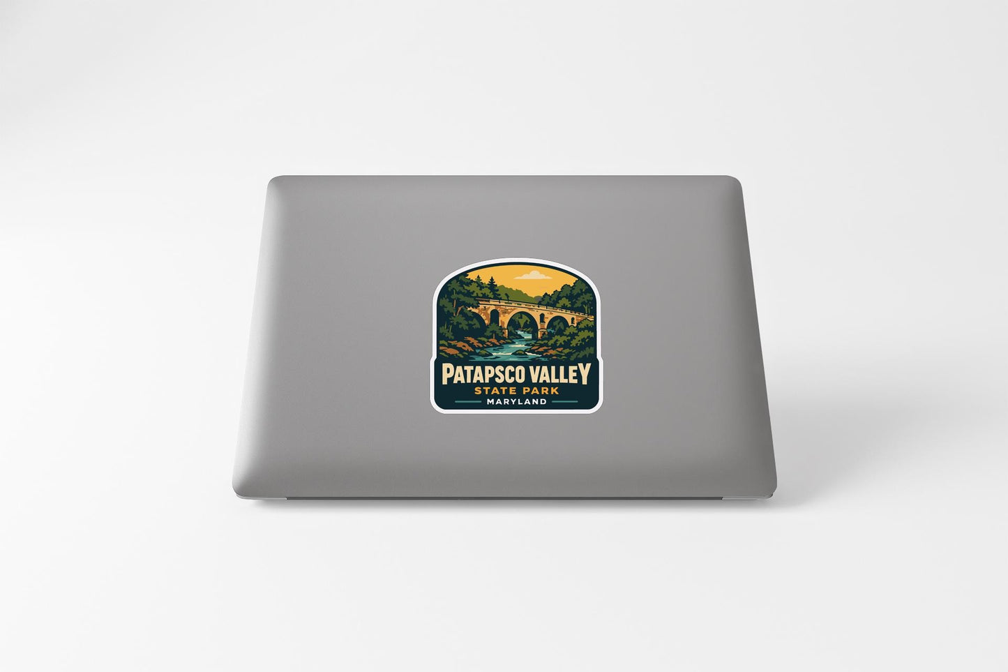 A sticker on the back of a laptop, depicting a scenic landscape with a bridge and trees.