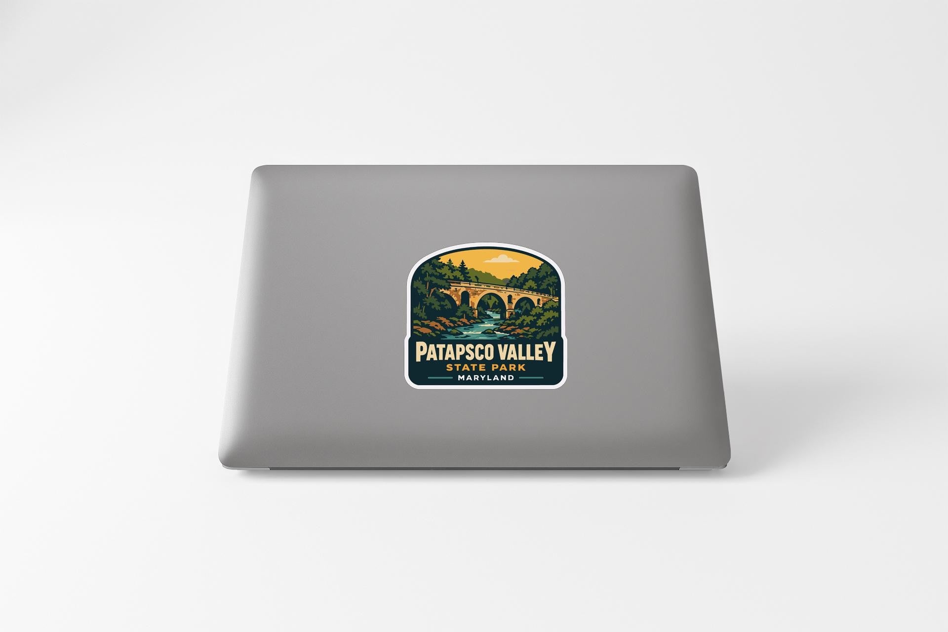 A sticker on the back of a laptop, depicting a scenic landscape with a bridge and trees.
