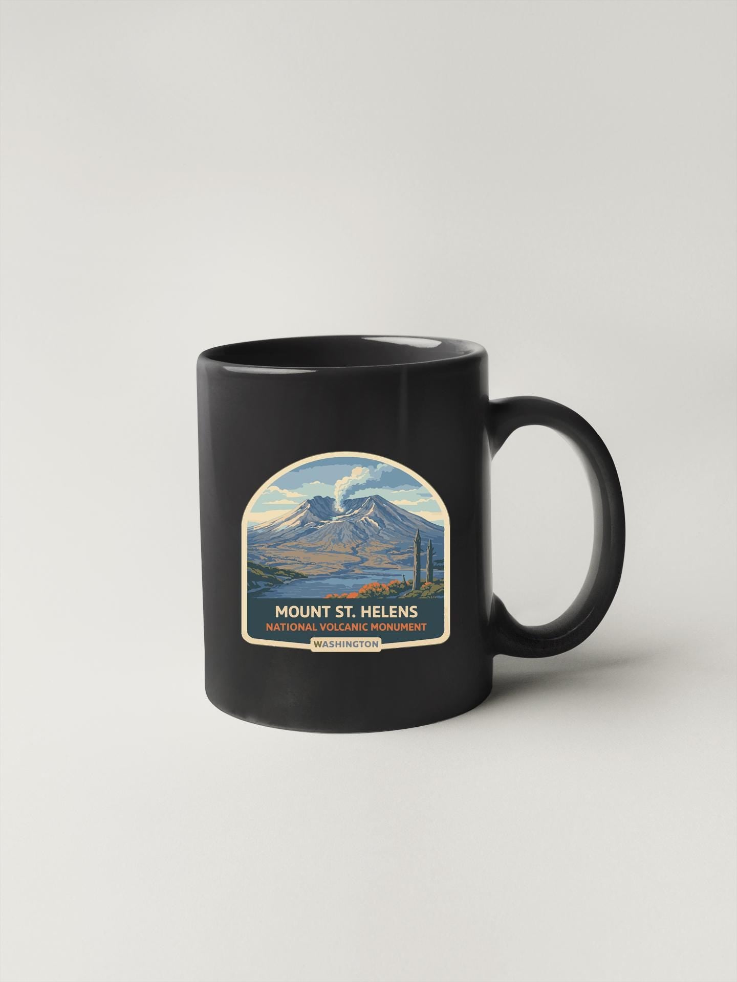 A black coffee mug with a graphic design depicting Mount St. Helens, a famous national volcanic monument.