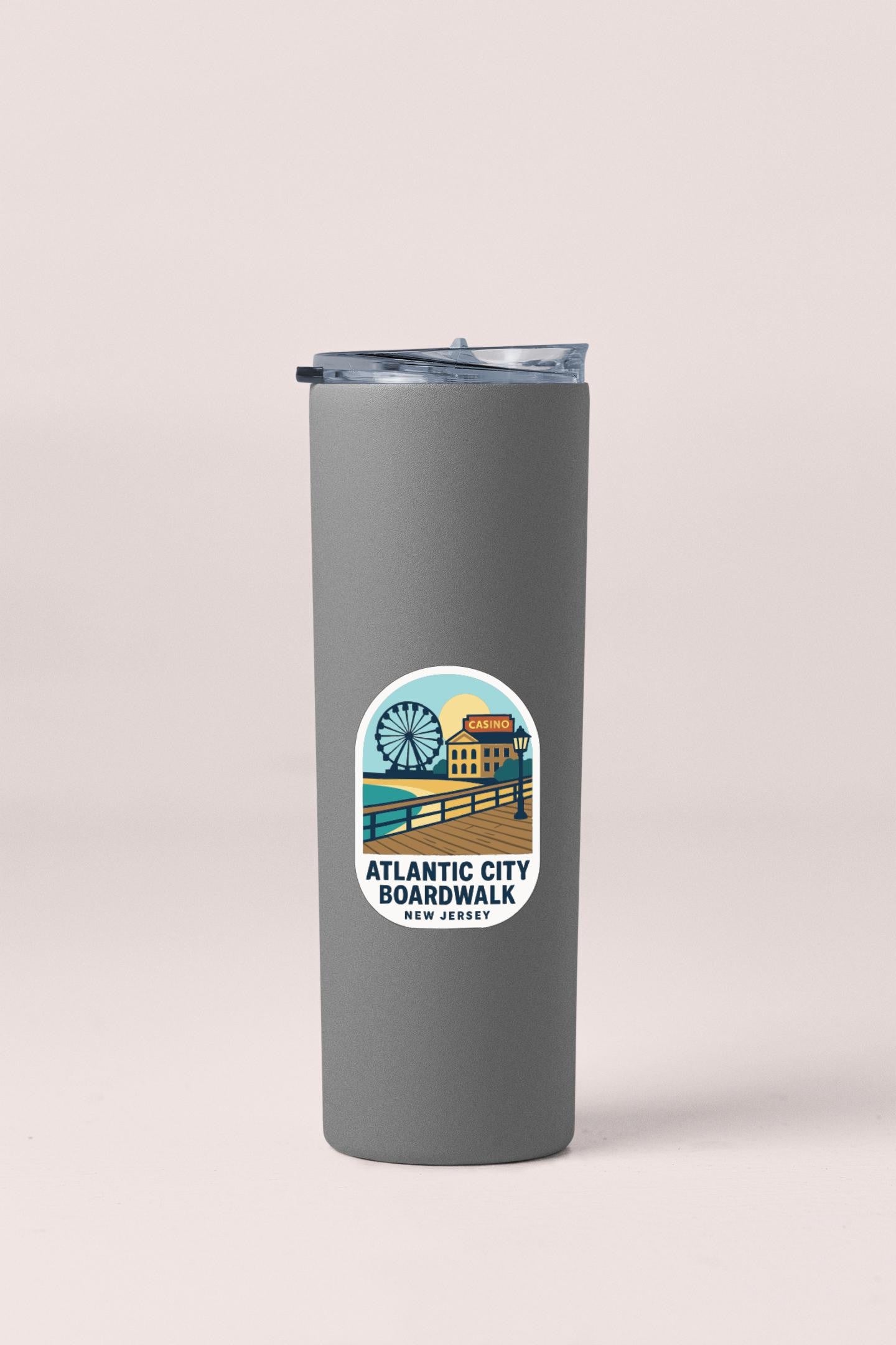 A gray insulated tumbler with a lid and a circular logo on it, featuring an illustration of the Atlantic City Boardwalk.