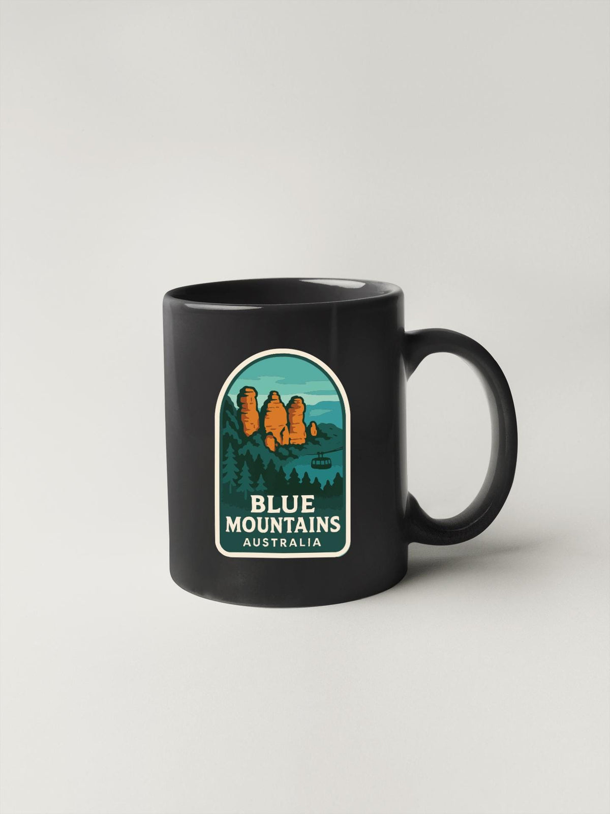 A black coffee mug with a graphic design depicting a scenic landscape with mountains and a lake, along with the text "BLUE MOUNTAINS AUSTRALIA".