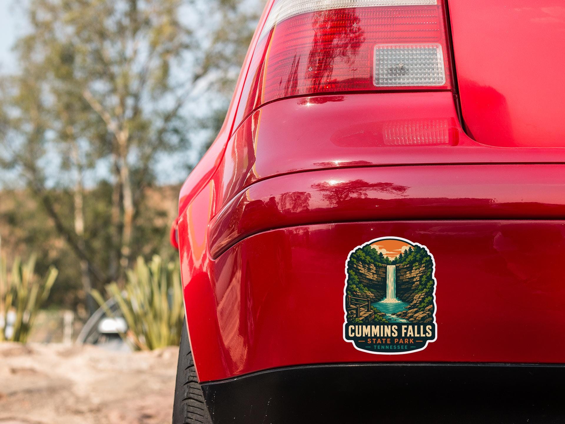 the rear end of a red car with a sticker on the trunk that says "Cummins Falls, Tennessee".