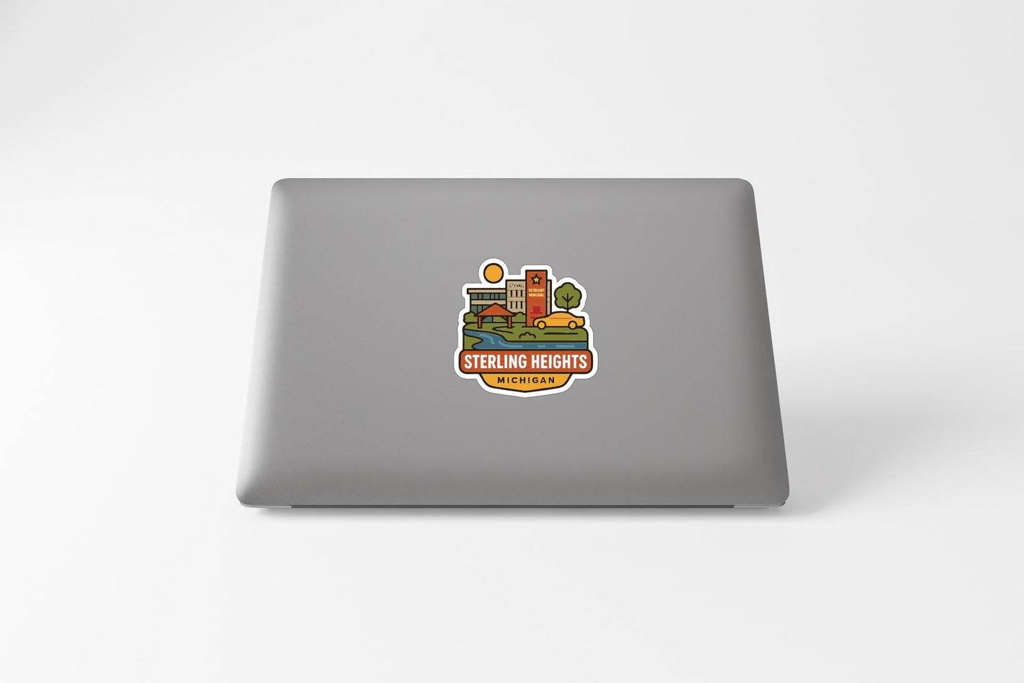 a sticker with a colorful illustration of a cityscape and the text "STERLING HEIGHTS CHICAGO" on the back of a laptop.