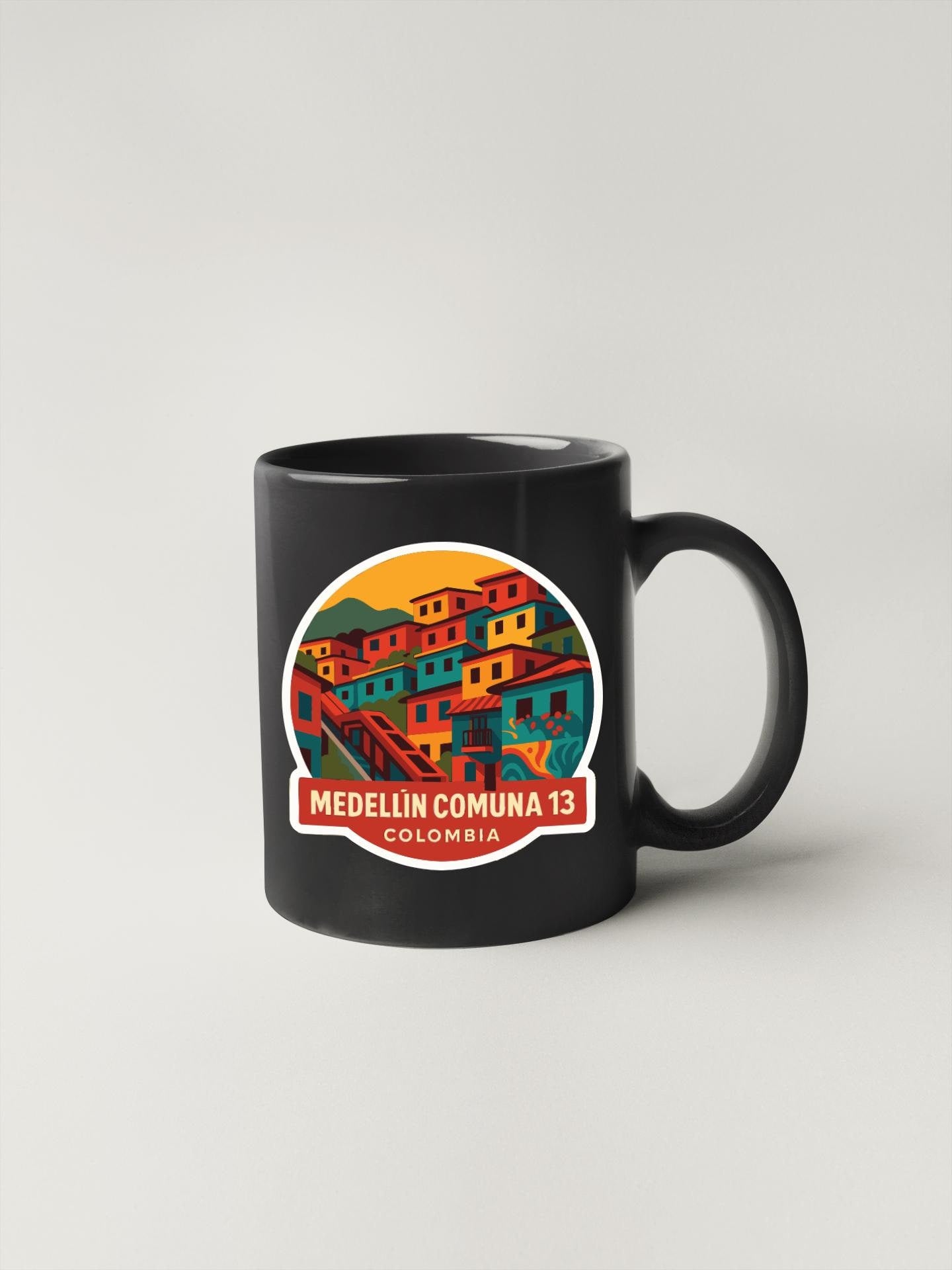 A black coffee mug with a colorful illustration of a town or village on it, along with the text "MEDELLÍN COMÌNÍA 13 COLOMBIA".