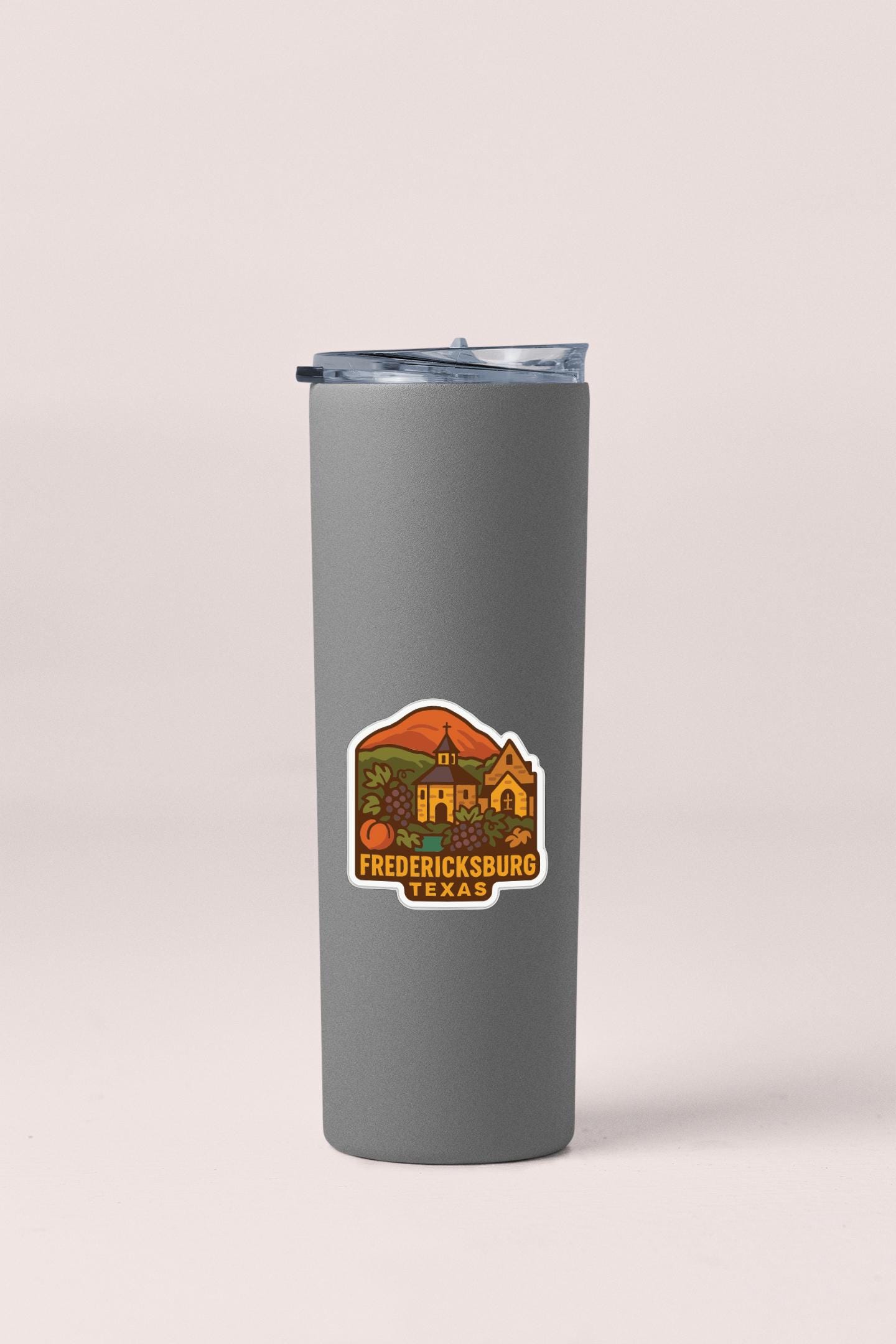 A gray insulated tumbler with a sticker depicting a scenic view of Fredericksburg, Texas.